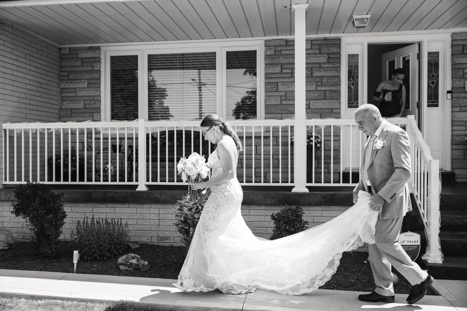 A black and white photo of a wedding party walking down porch steps.