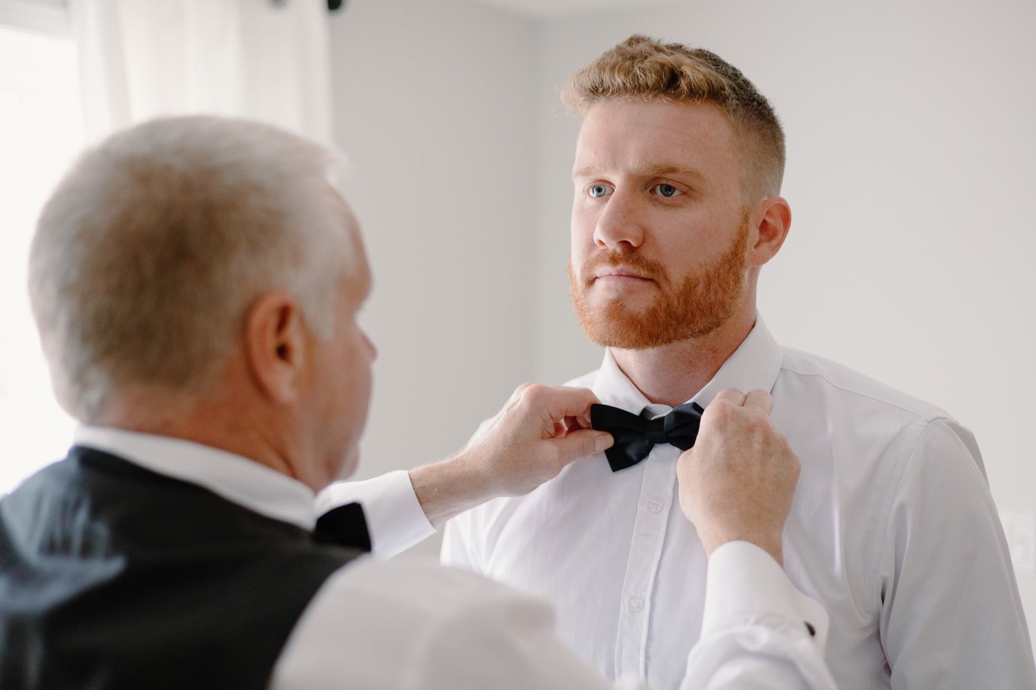A bow tie is being adjusted on a person wearing a crisp white shirt.