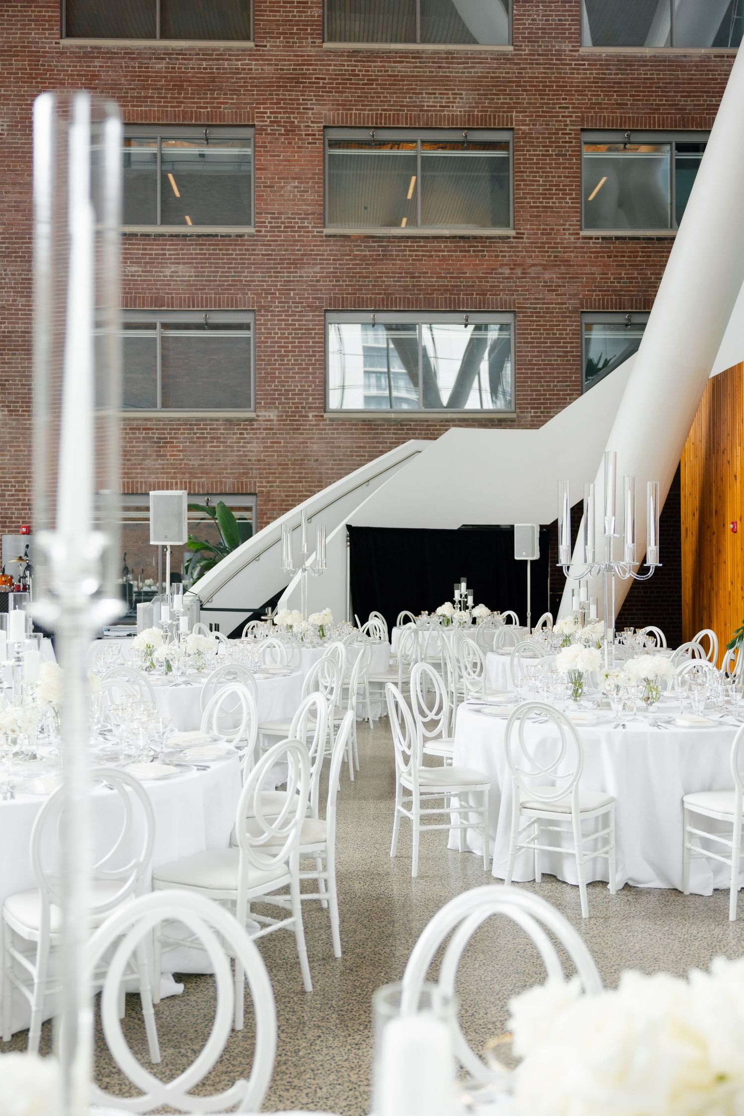 Modern wedding reception space with white round tables and chairs set against industrial brick walls.