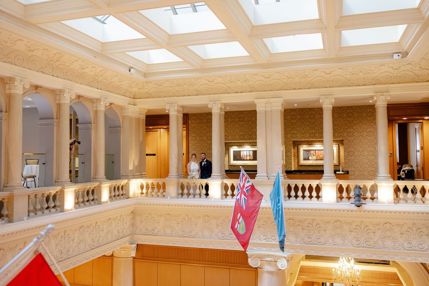 Grand interior hallway with skylight windows and classical columns featuring red and blue hanging banners.