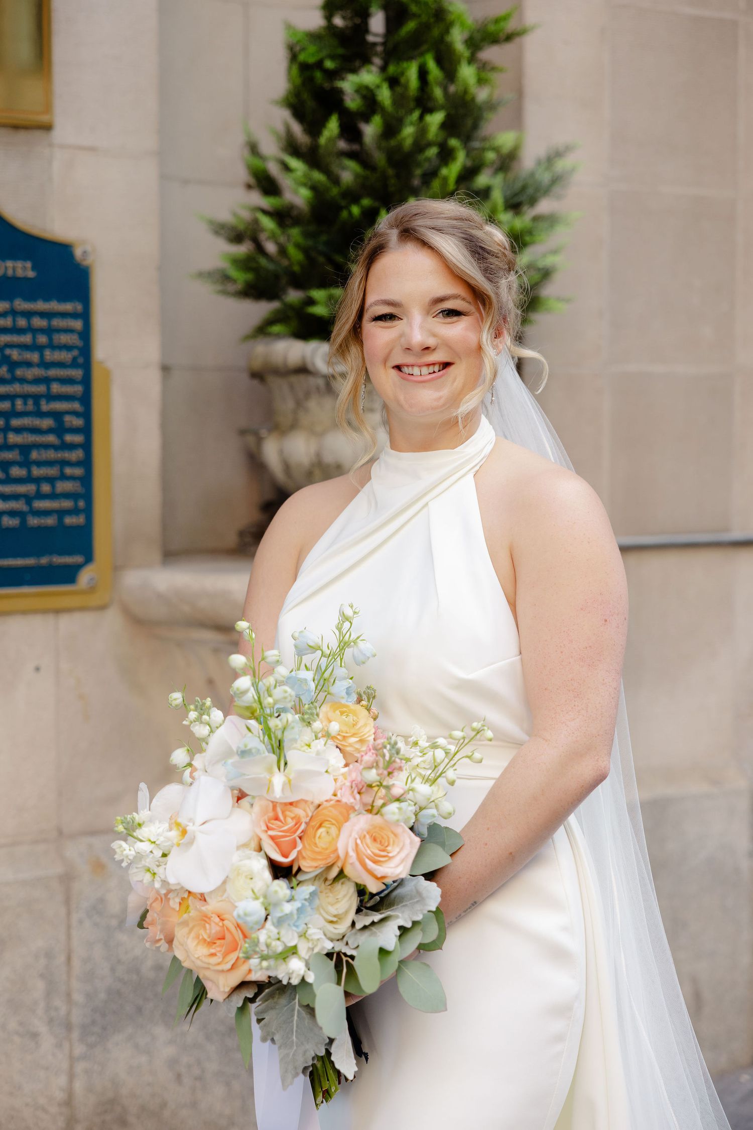 Beautiful wedding bouquet with peach roses, white flowers and eucalyptus against a white bridal gown.