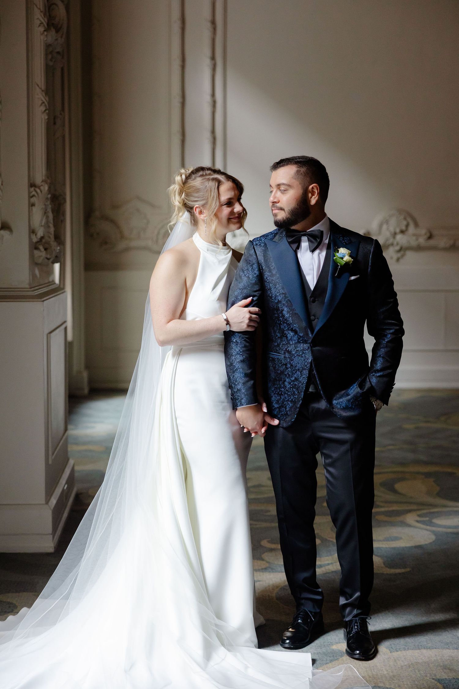 Romantic wedding couple shares intimate moments in an elegant hallway with ornate molding and natural lighting.