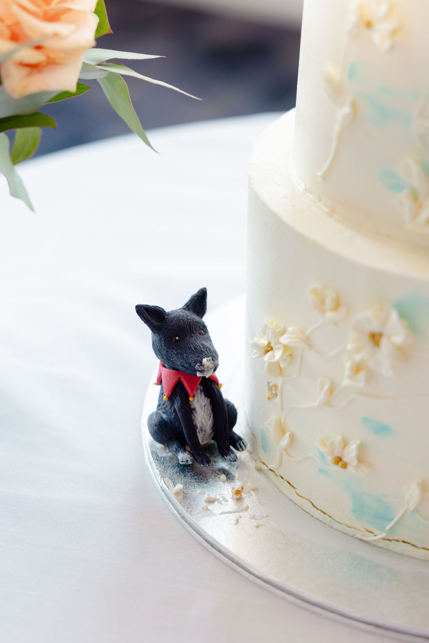 Close-up detail of a white wedding cake decorated with a small black dog figurine wearing a red bow tie.