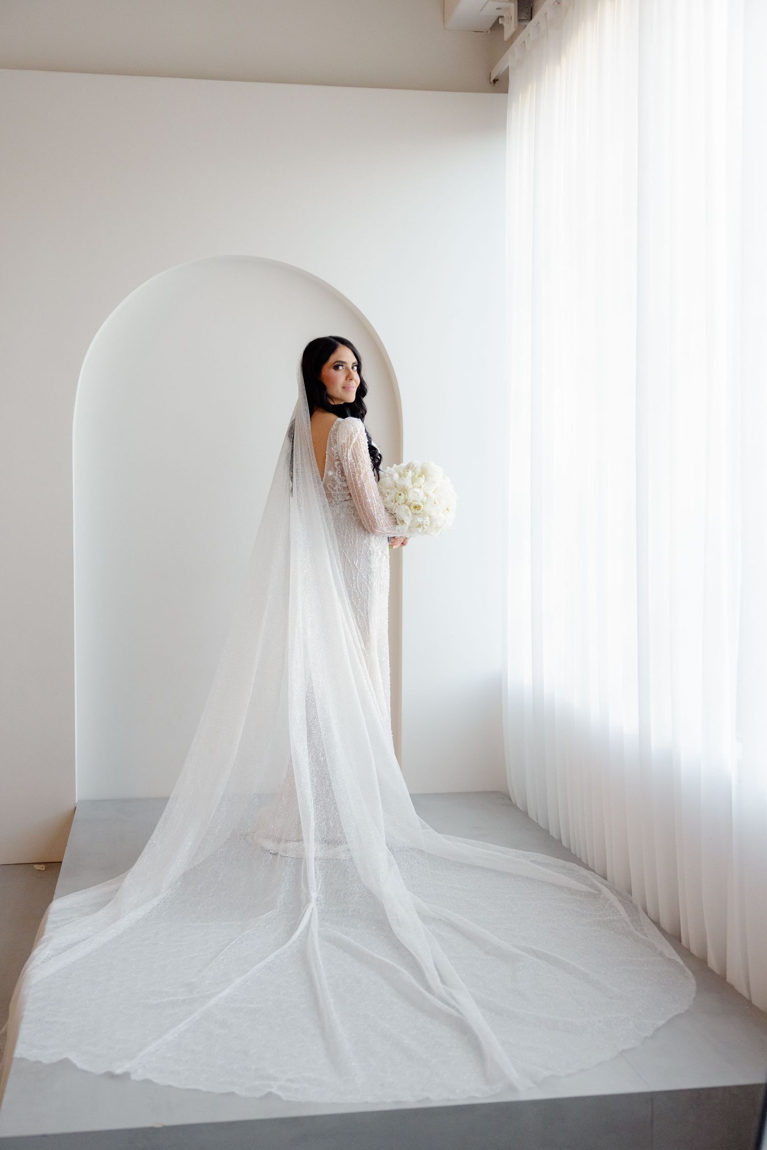 Cathedral length veil trails behind bride in elegant white archway setting.