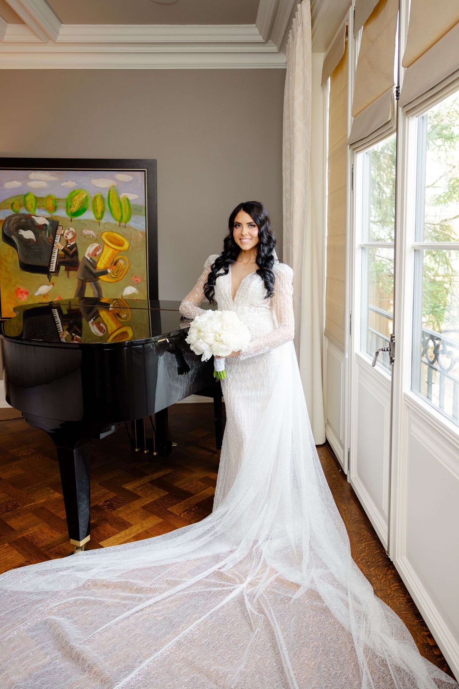 Stunning bridal photo with flowing cathedral veil next to grand piano.
