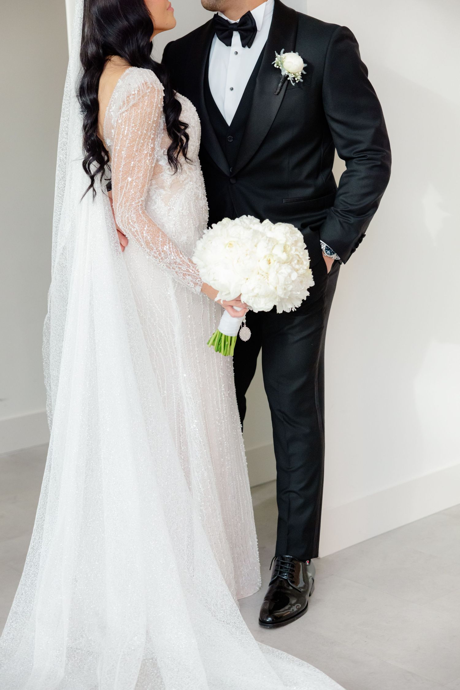 Close up of bride in lace gown and groom in tuxedo with white floral bouquet.