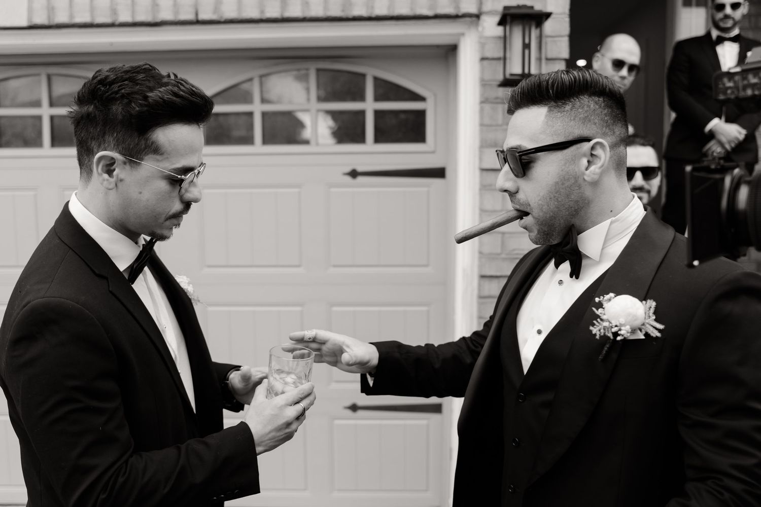 Black and white photo of groomsmen in tuxedos exchanging items before the wedding.