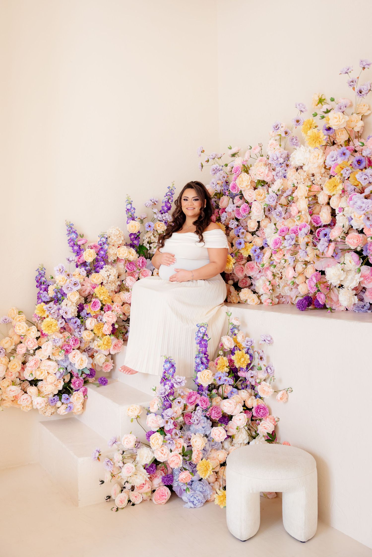 A sweeping floral arrangement in purple and peach tones frames a dreamy white studio portrait setting.