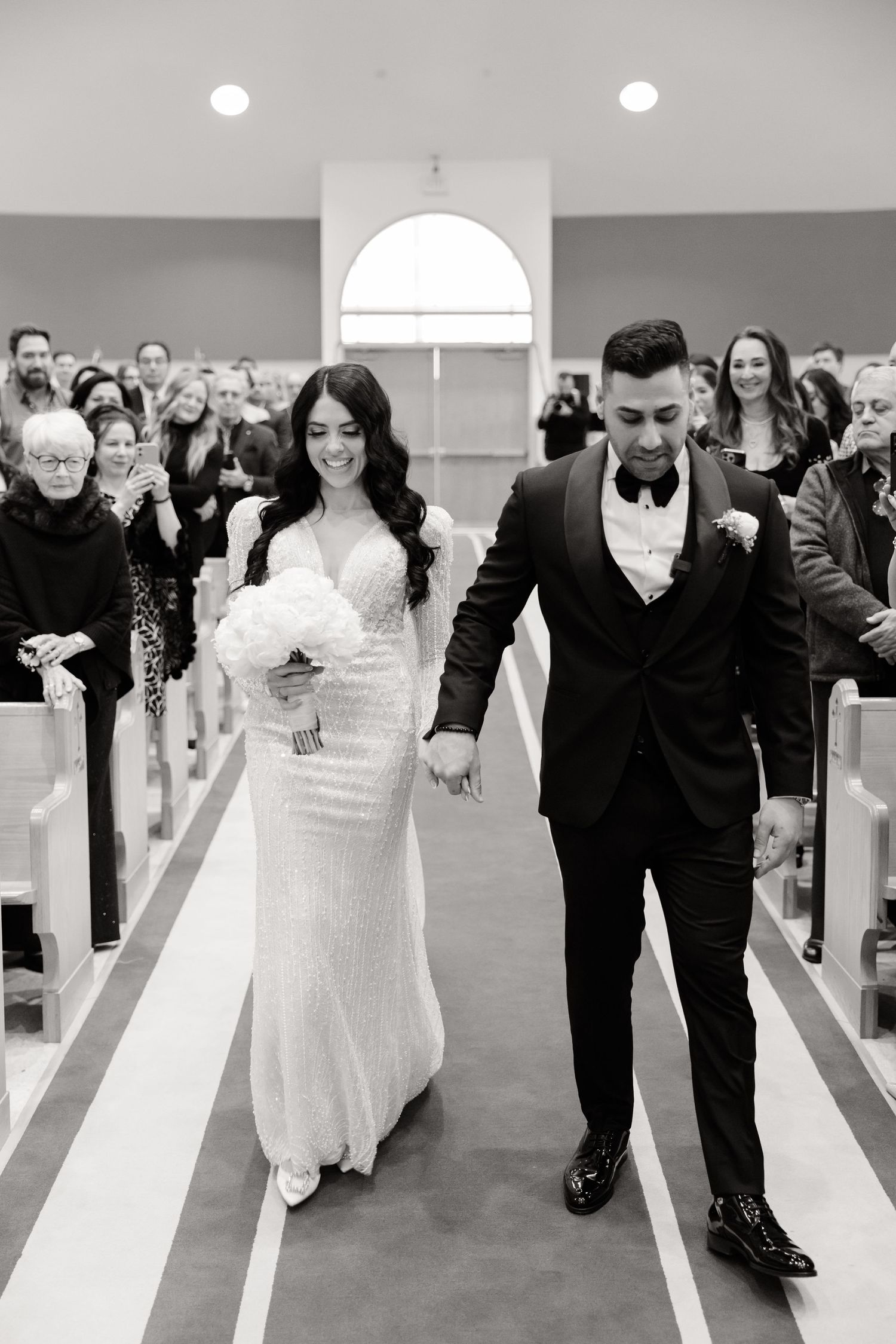 A couple walks down the aisle together while wedding guests look on in a church ceremony.