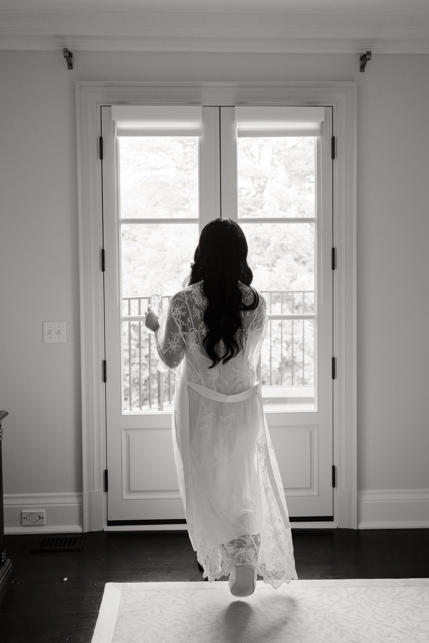 A figure in a flowing white dress moves contemplatively through a series of black and white photos near a window.
