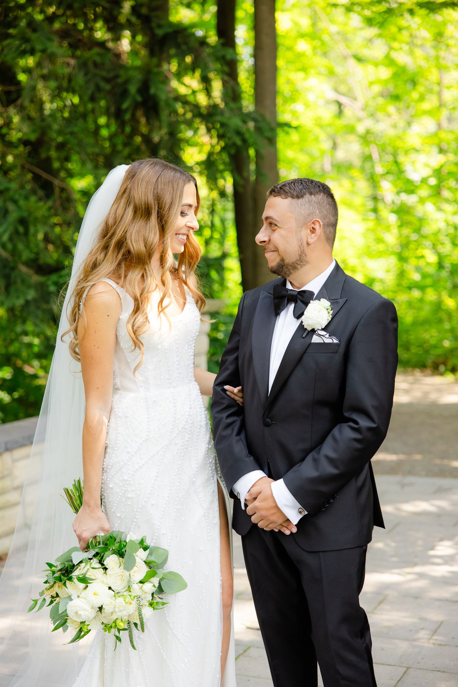 Bride in white gown and groom in tuxedo share intimate moment on garden path.