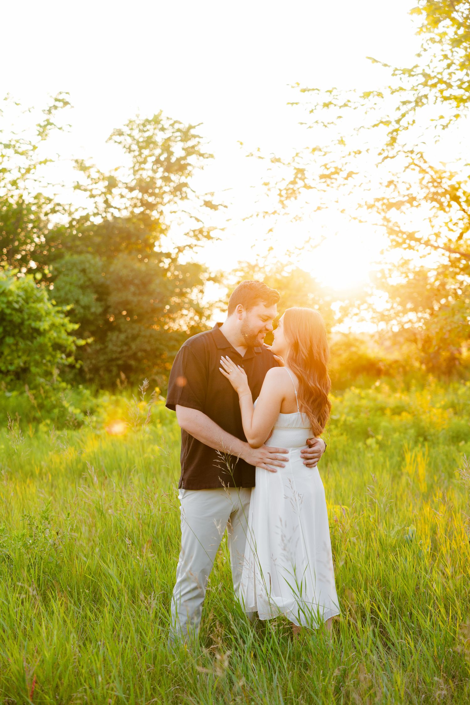 Intimate moment between couple in summer meadow with dramatic sunset lighting.