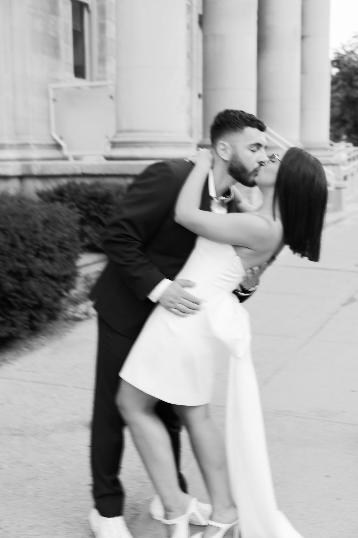 Intimate black and white portrait of couple embracing on steps of classical building.