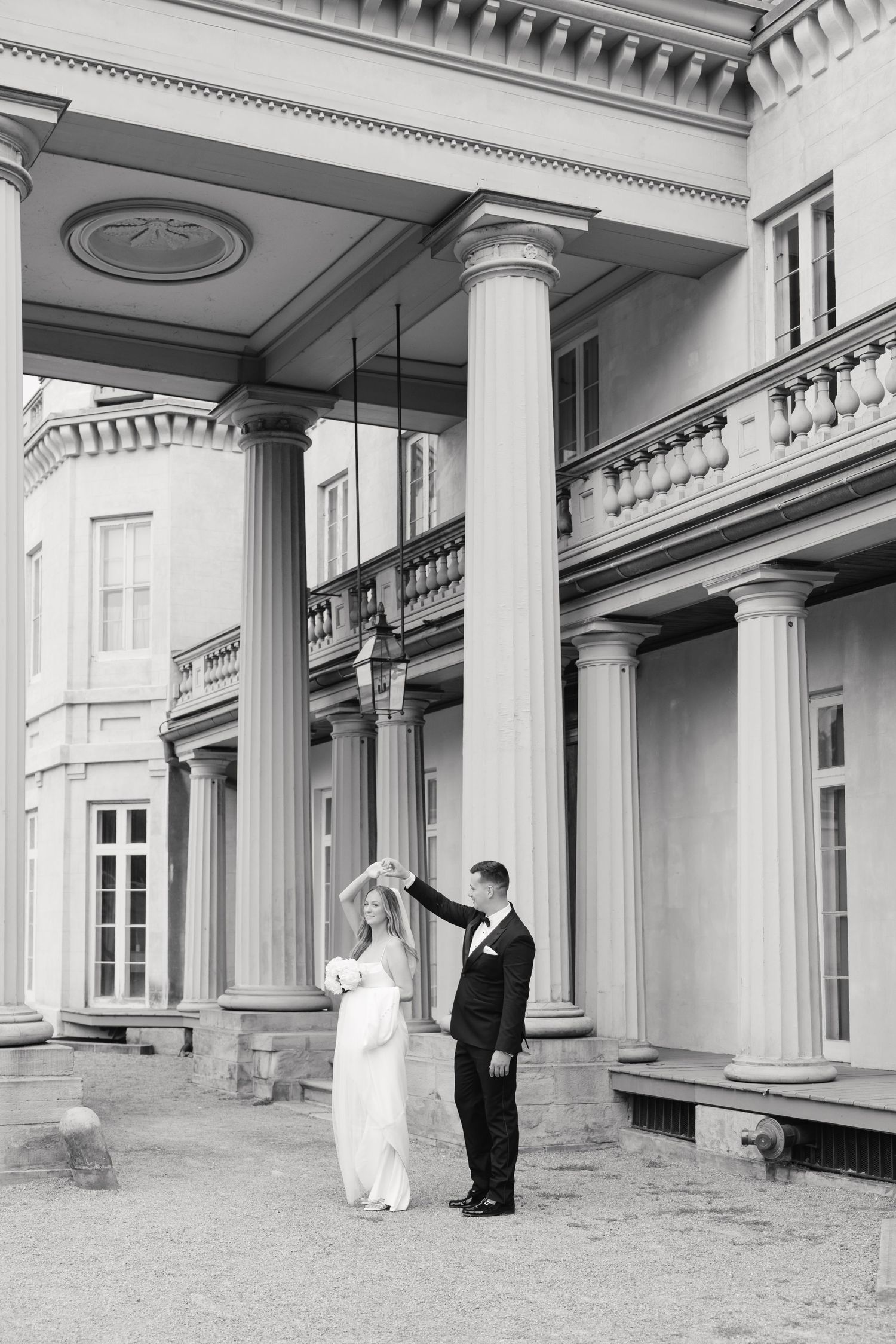 Black and white photo of couple dancing under grand columned portico of historic mansion.