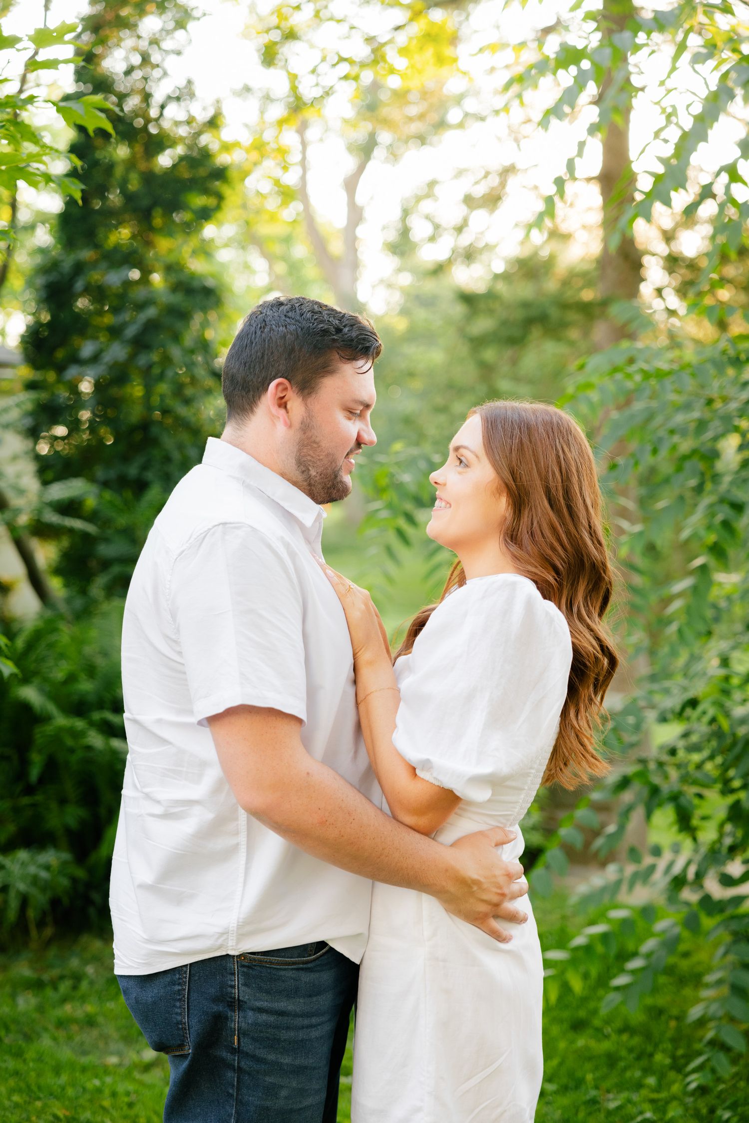 Couple in matching white outfits sharing an intimate moment in a sun-dappled garden.