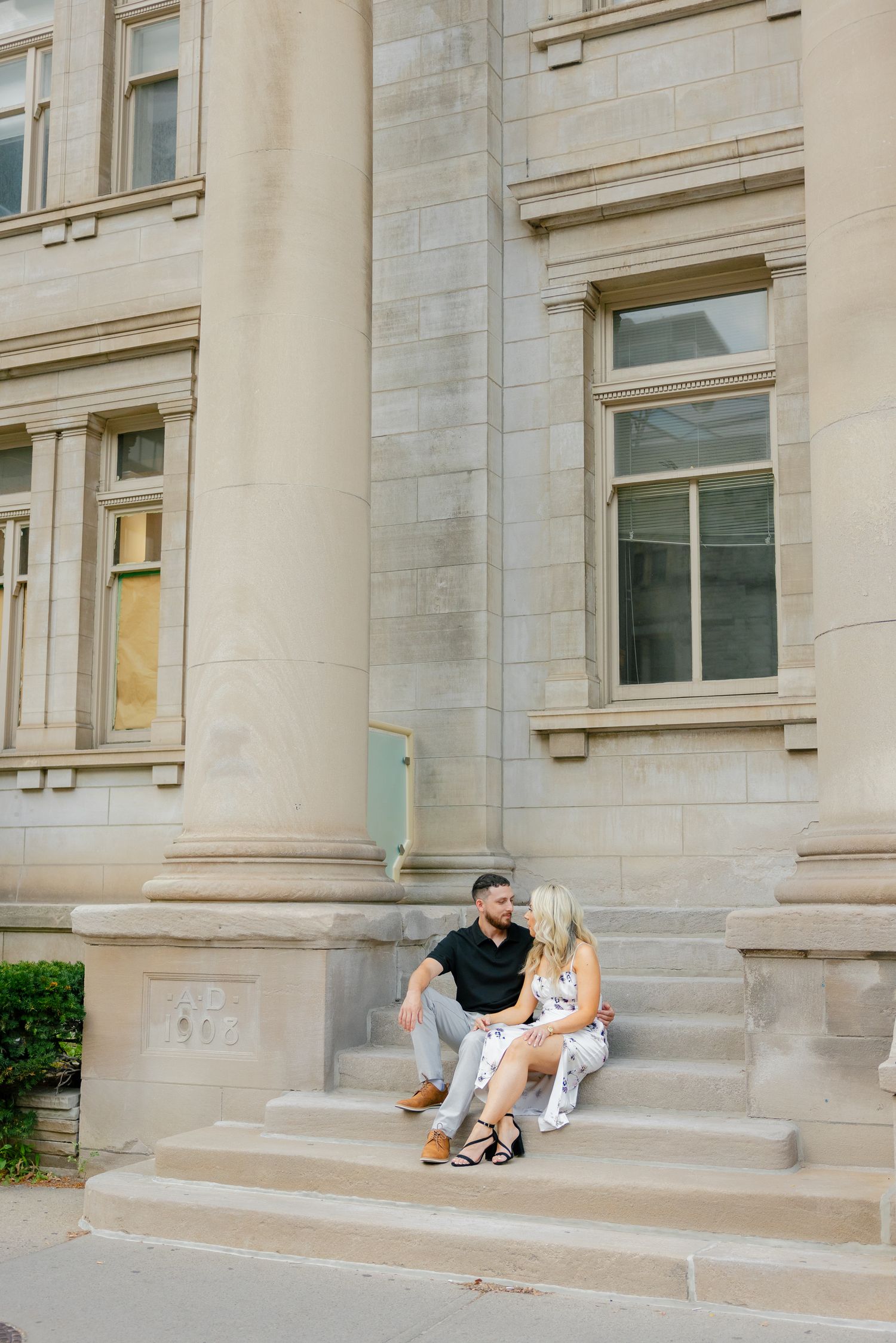A couple sits together on exterior steps of a grand stone building.