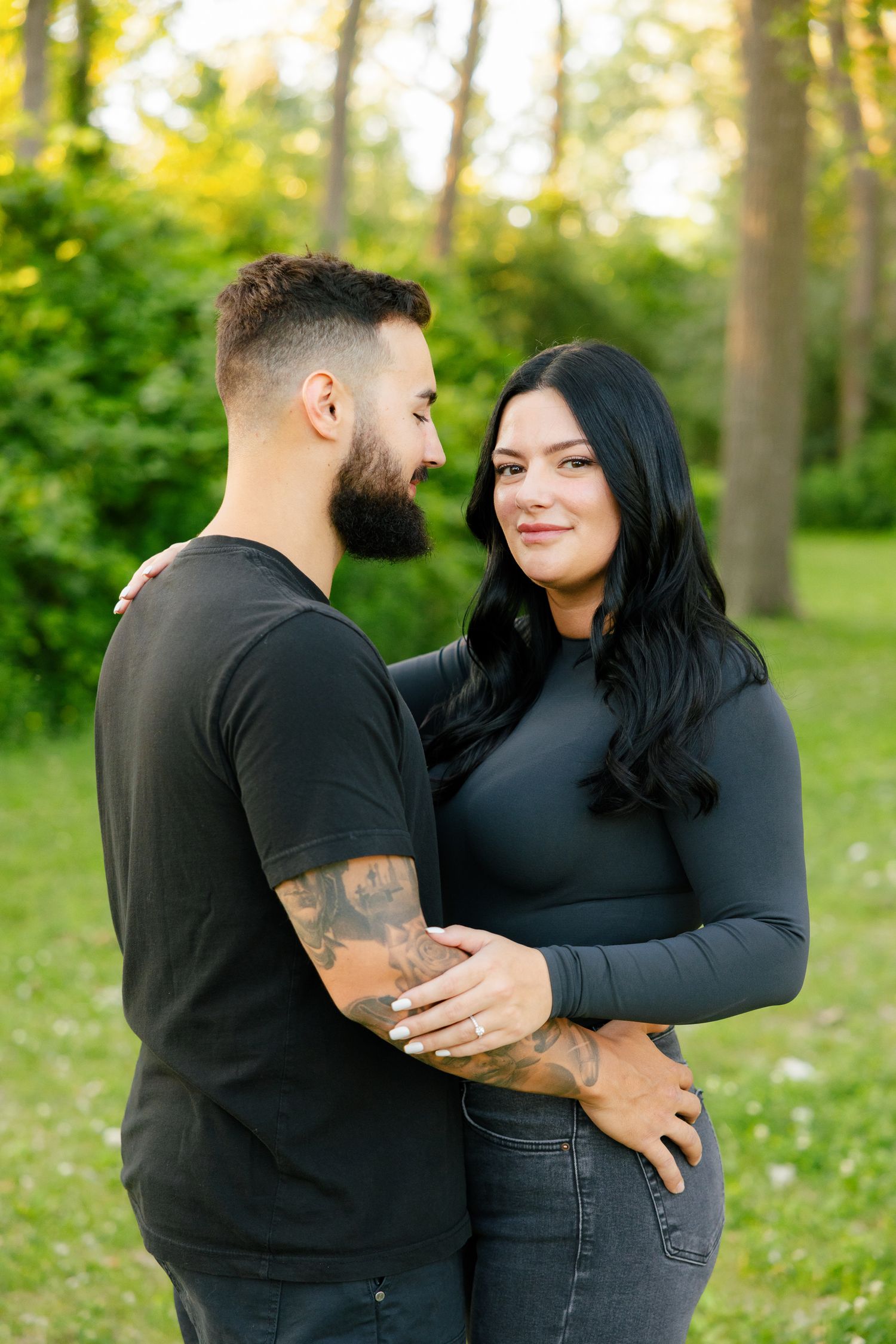 Loving couple in matching black outfits share an embrace in a peaceful woodland garden.