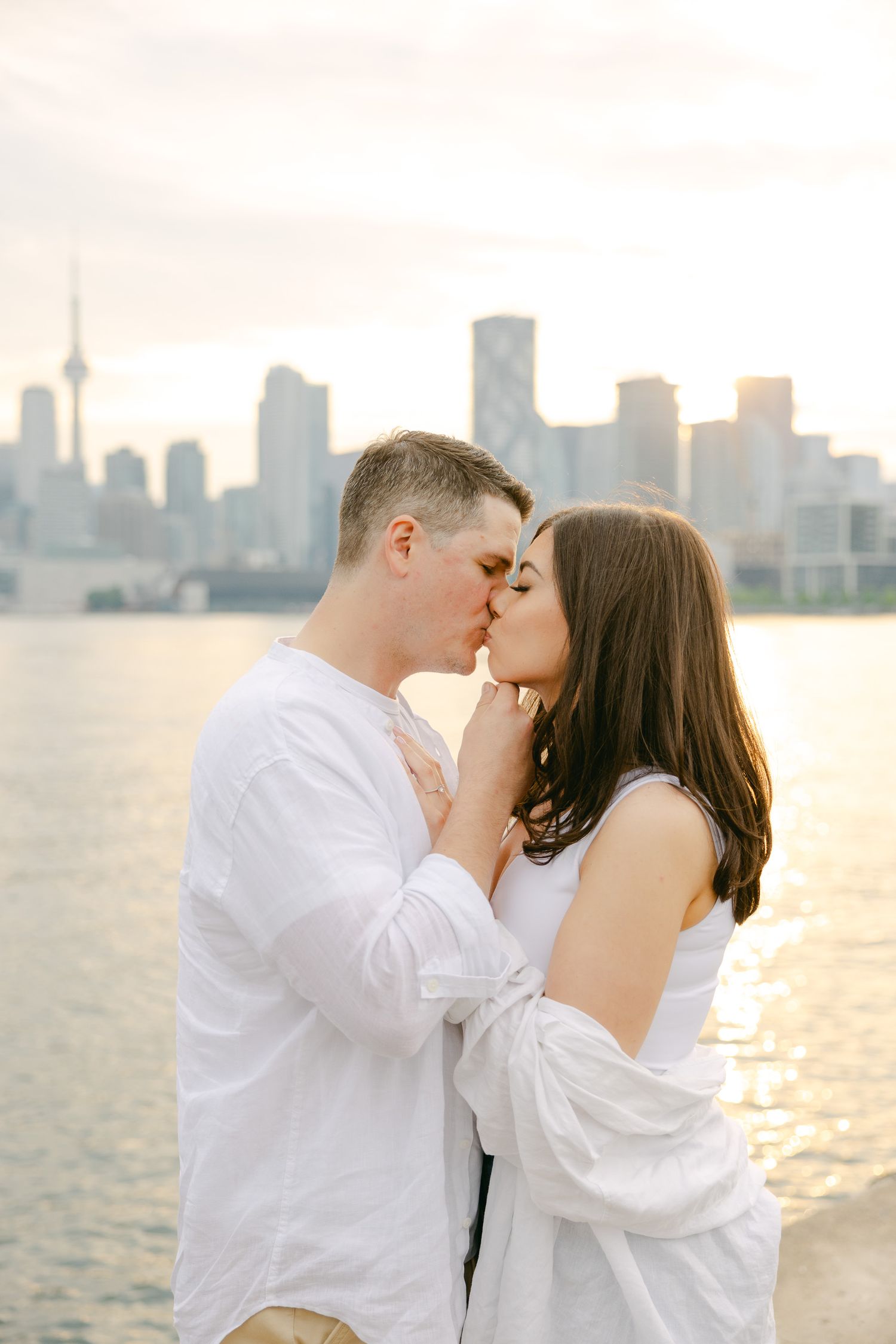 A romantic kiss captured at sunset with Toronto's skyline creating a stunning backdrop.