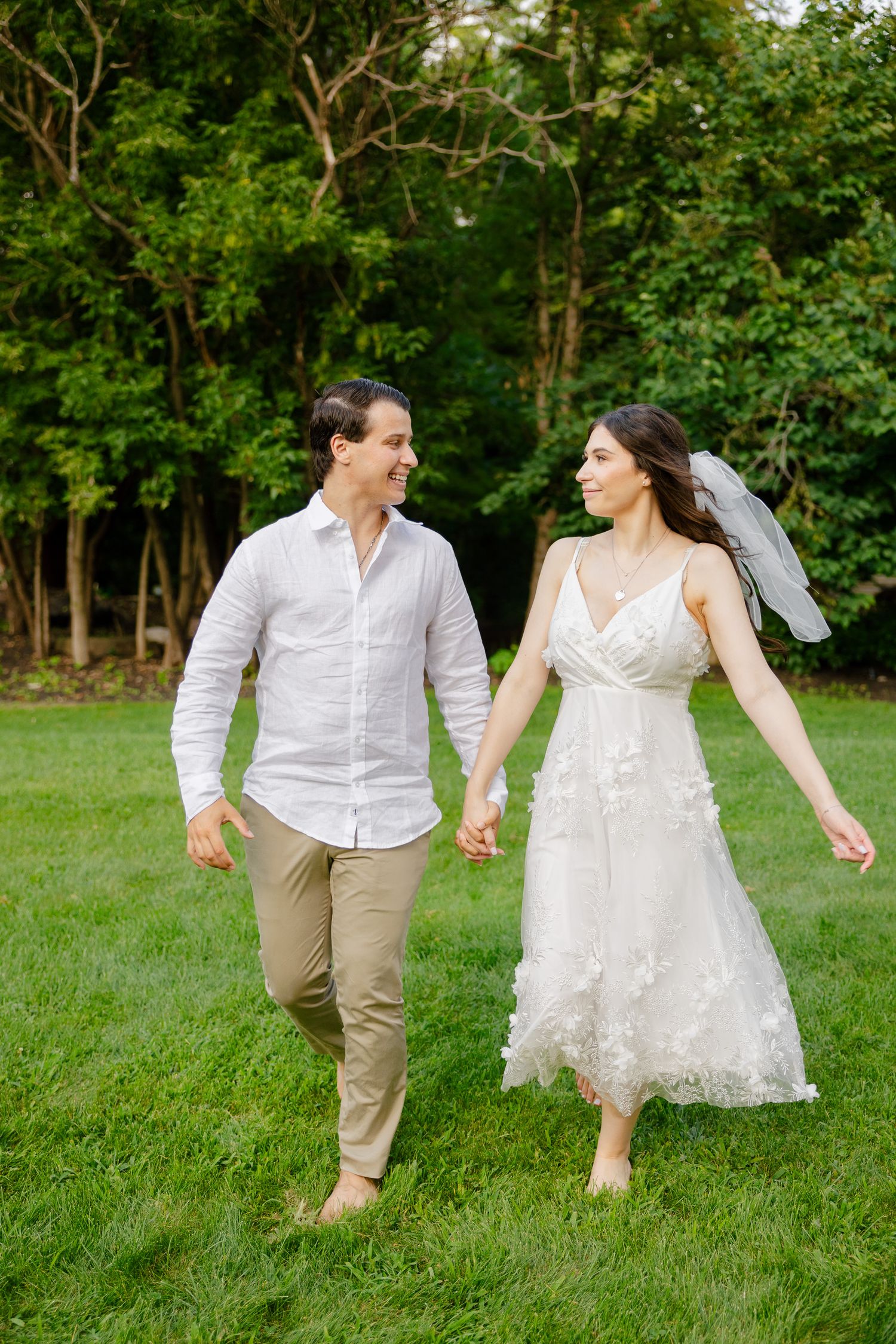 A couple walking barefoot through a lush garden in wedding attire.