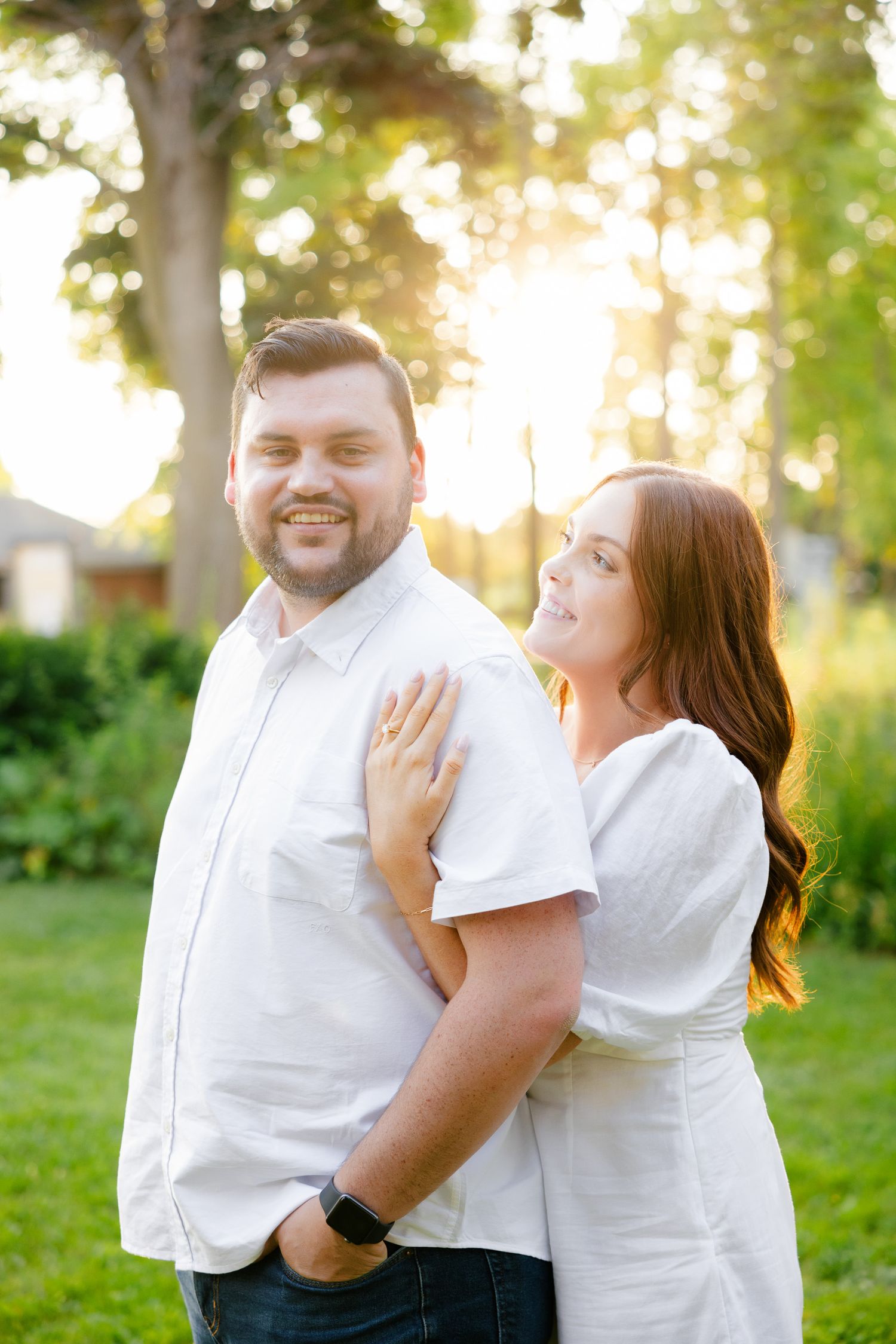 Happy couple in matching white outfits pose together in a sunlit outdoor setting.