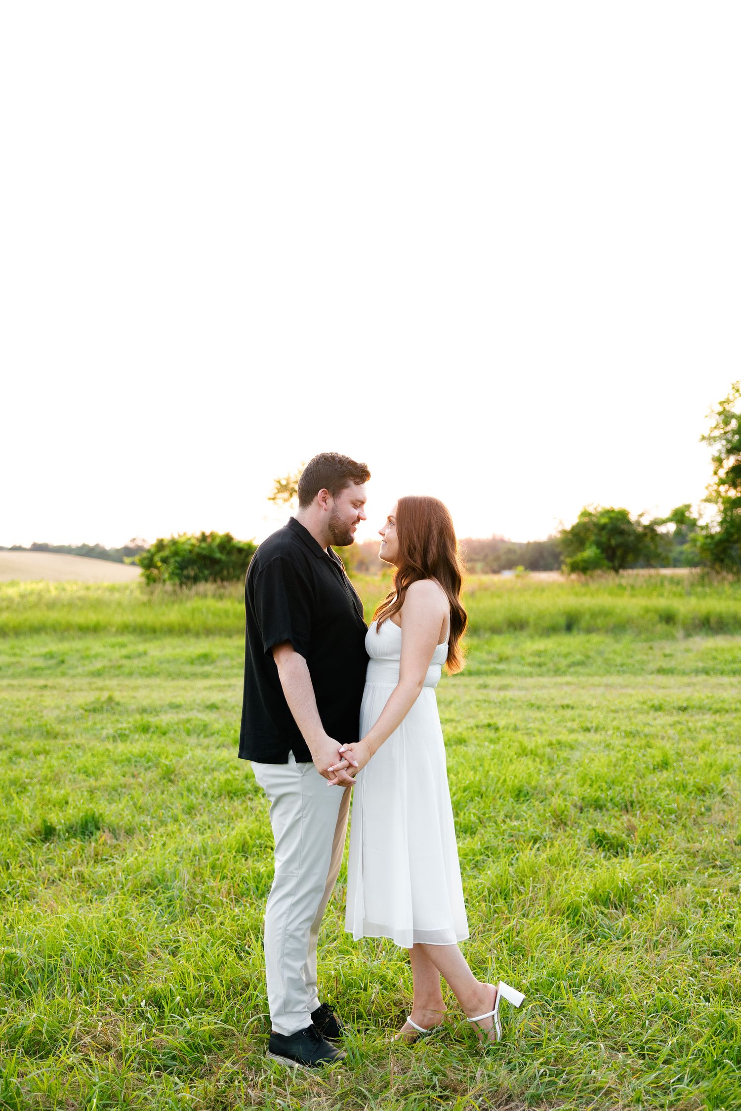 A romantic couple poses together in a grassy meadow during golden hour.
