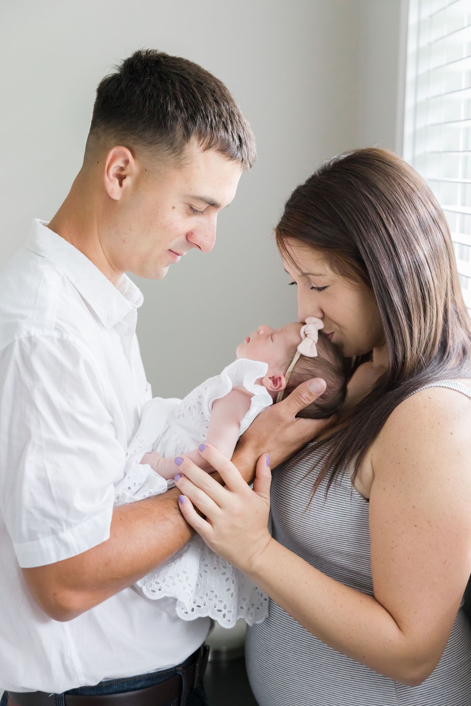 Parents share tender moment with newborn baby dressed in delicate white lace.