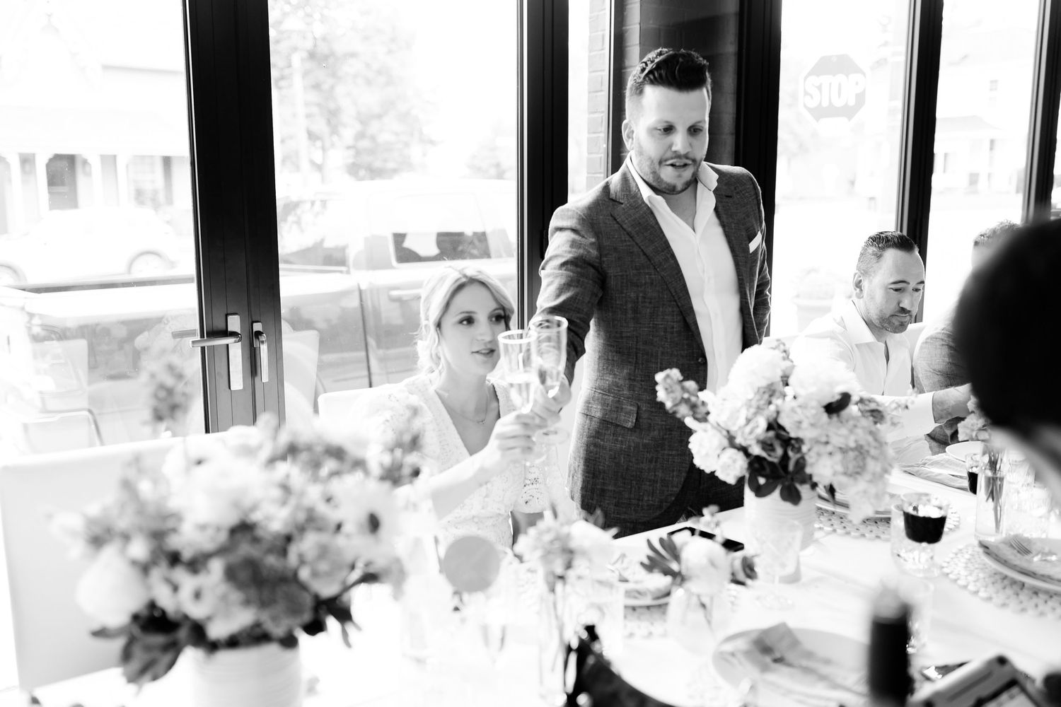 Black and white photograph of guests gathered around a dining table with floral centerpieces.