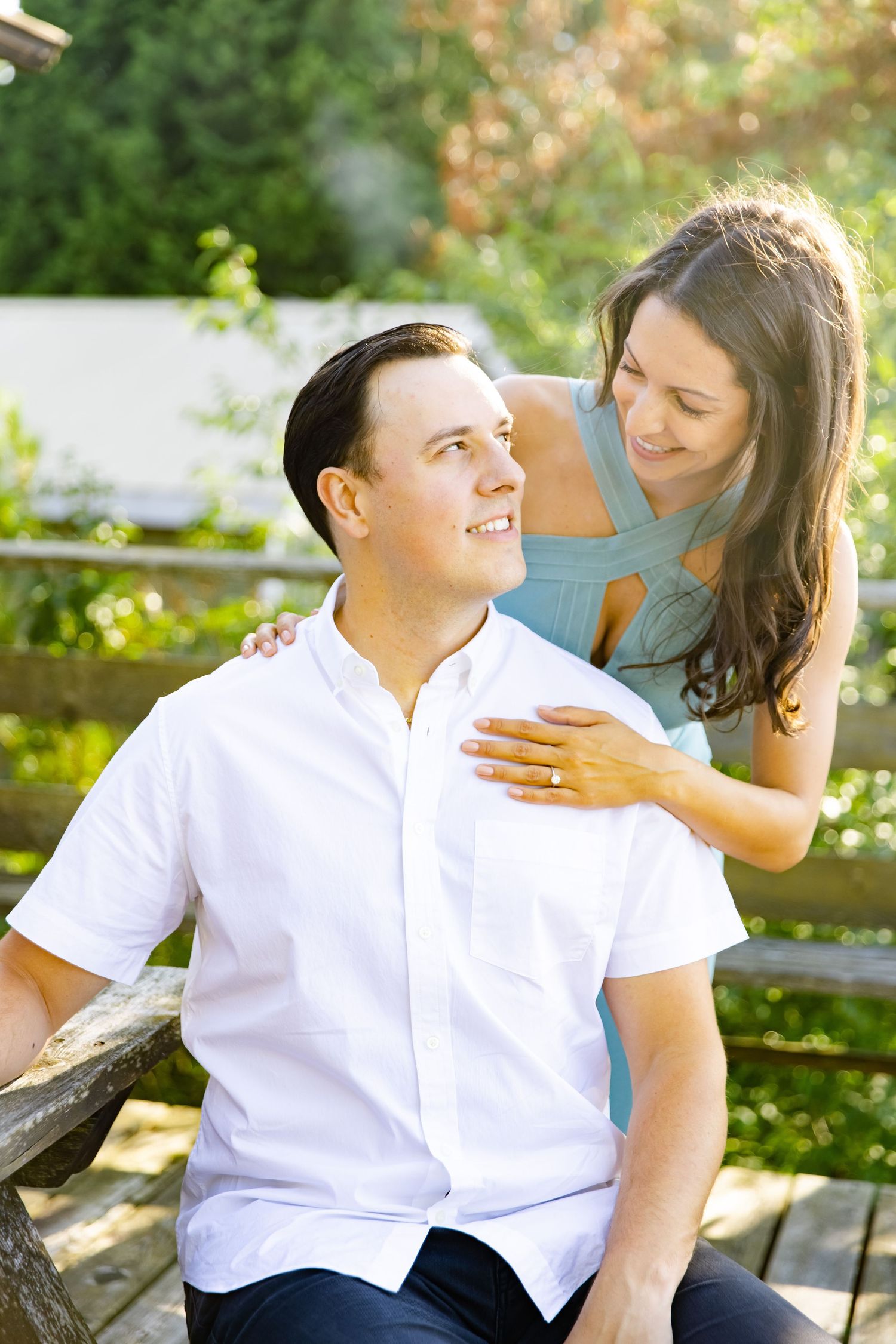 A romantic outdoor photo session with a couple in white shirt and blue dress against a sunlit garden backdrop.