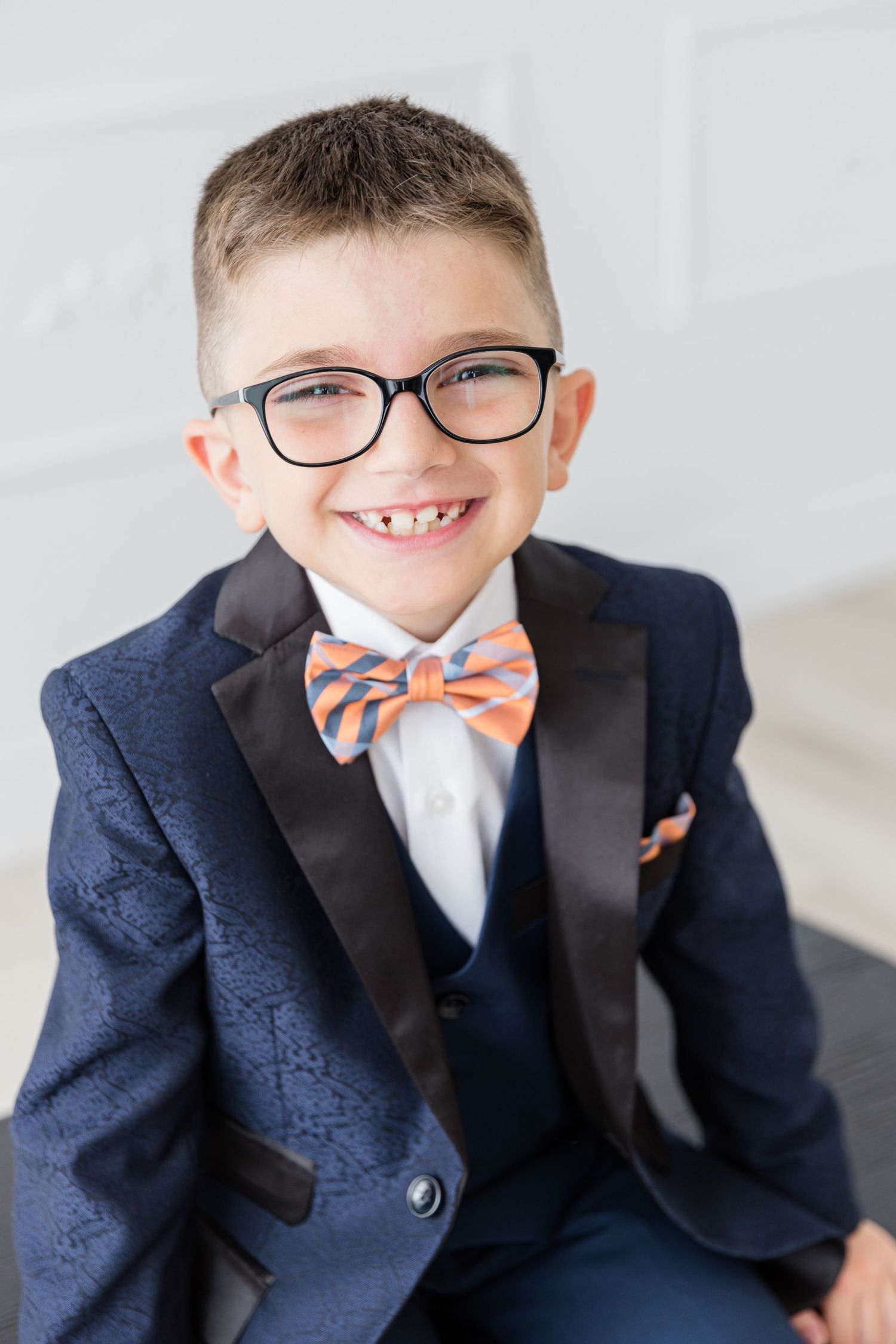 Close up portrait of youth in navy suit and glasses wearing orange and blue striped bowtie.