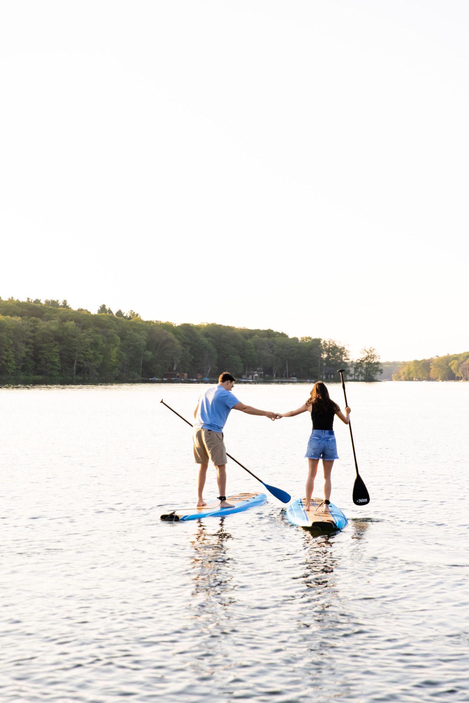 Couple holding hands while paddleboarding together on serene lake.