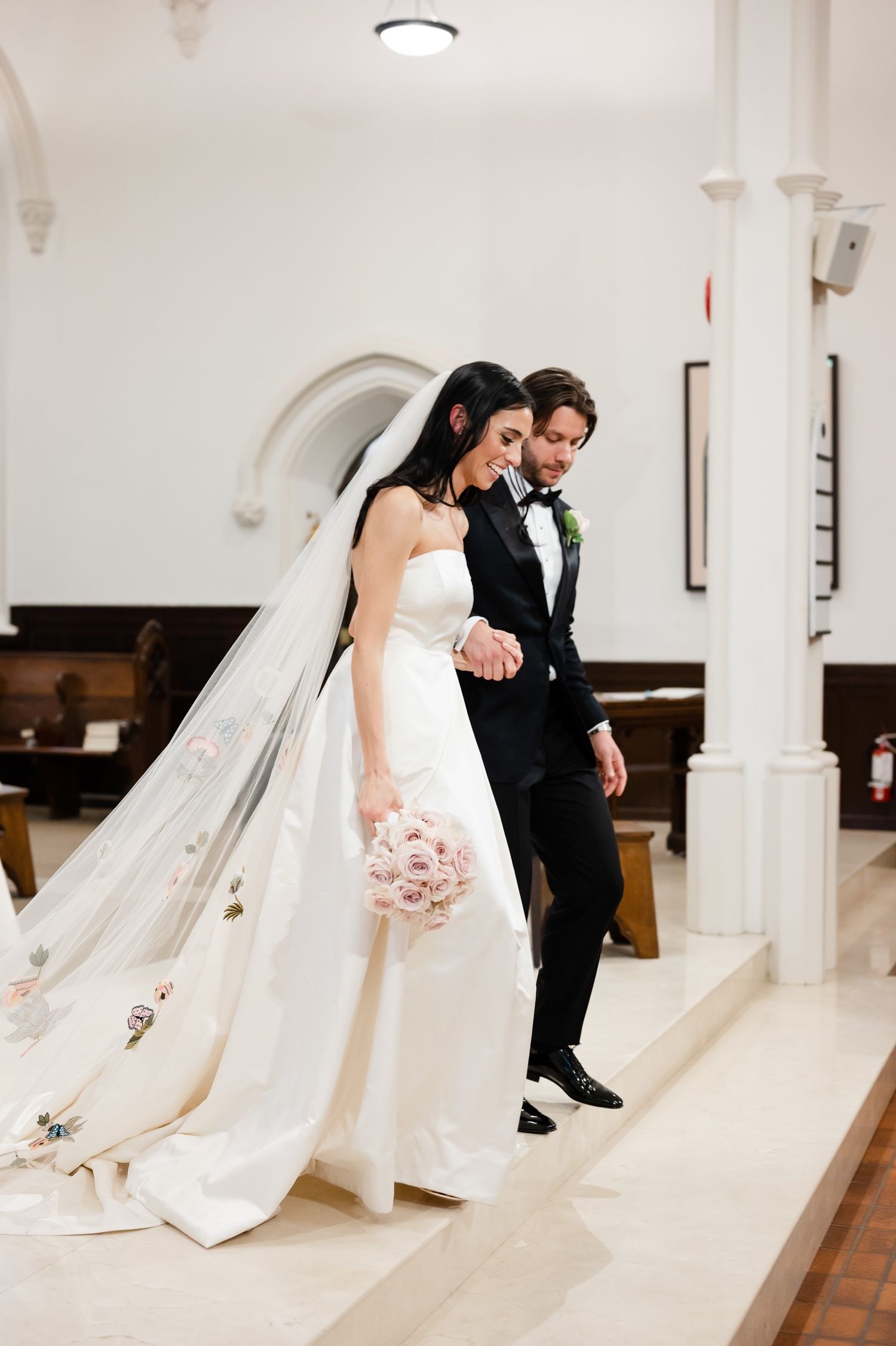 A couple shares a tender moment in a church, with the bride holding a pink bouquet.