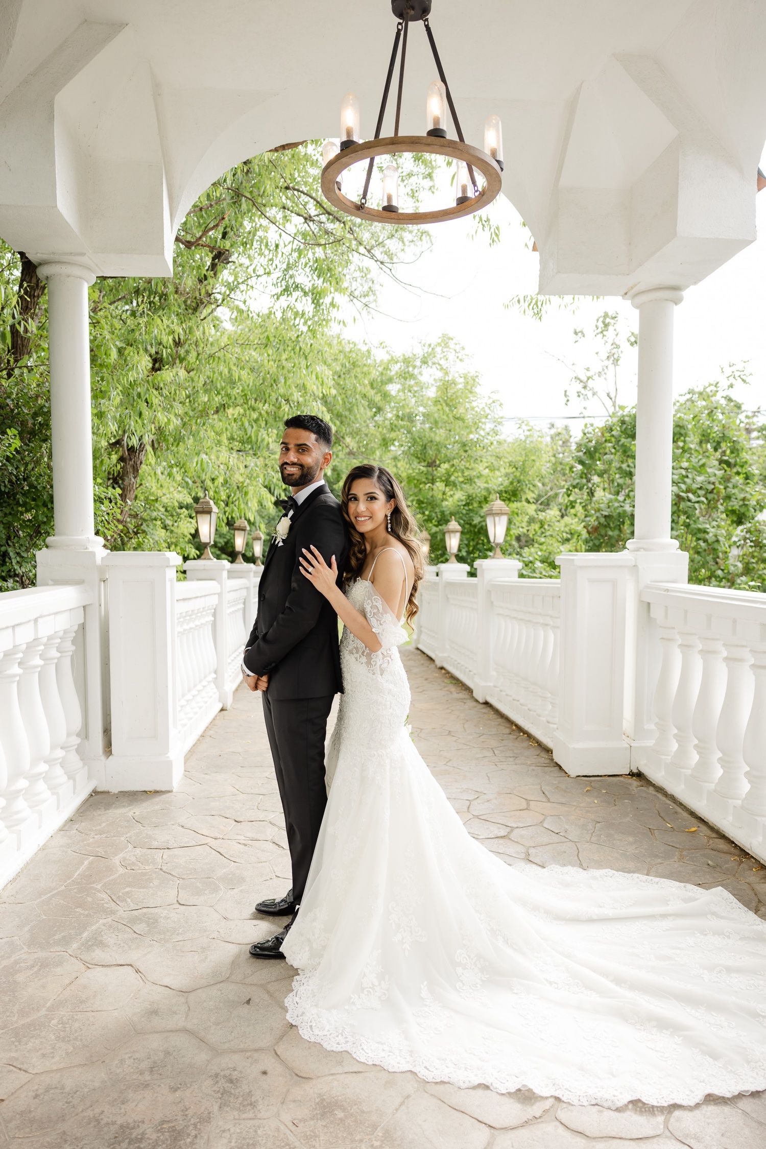 Newlyweds share joyful moment under arched white colonnade with trailing bridal gown.