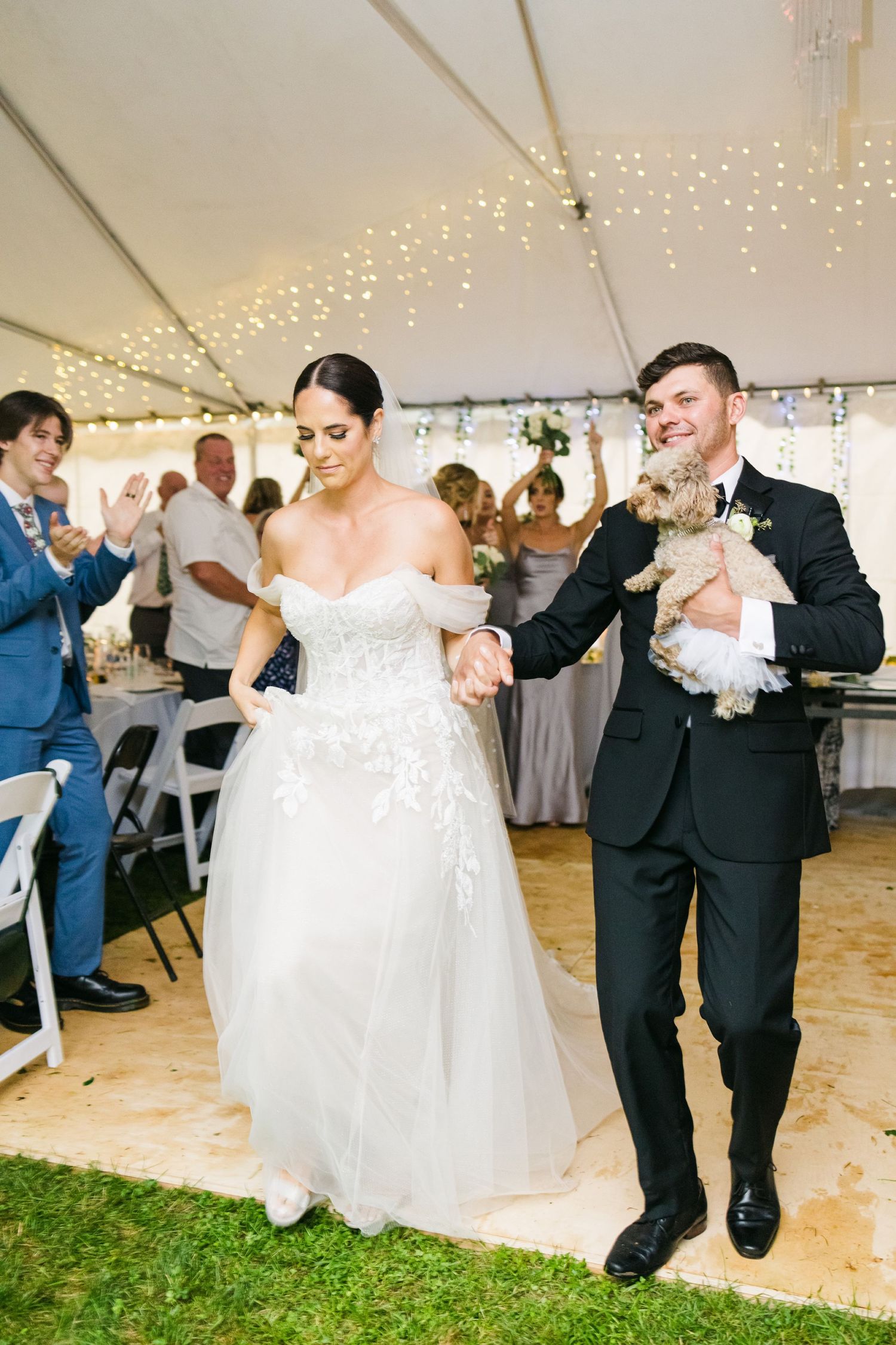 Newlyweds share their first dance under a tent decorated with twinkle lights at an outdoor wedding reception.