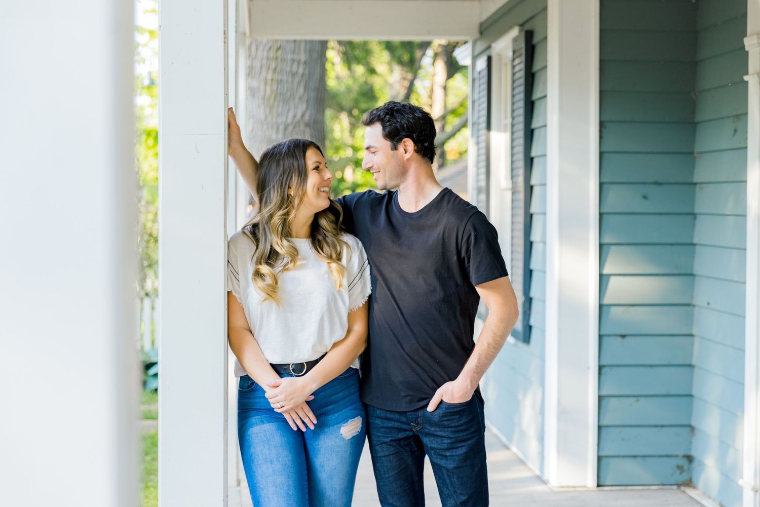 A couple shares a sweet moment while standing on a covered porch with white columns.