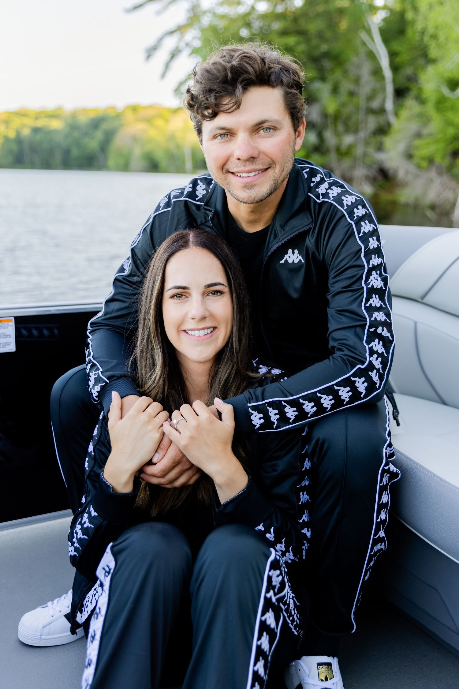 Couple wearing Kappa sportswear share tender moment while relaxing on boat cushions.