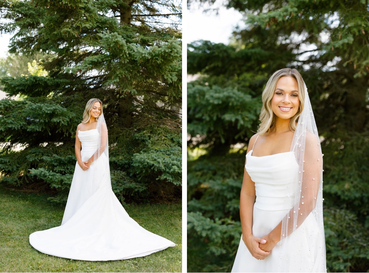 Bride in elegant white wedding gown with veil poses for portraits in front of tall evergreen trees.