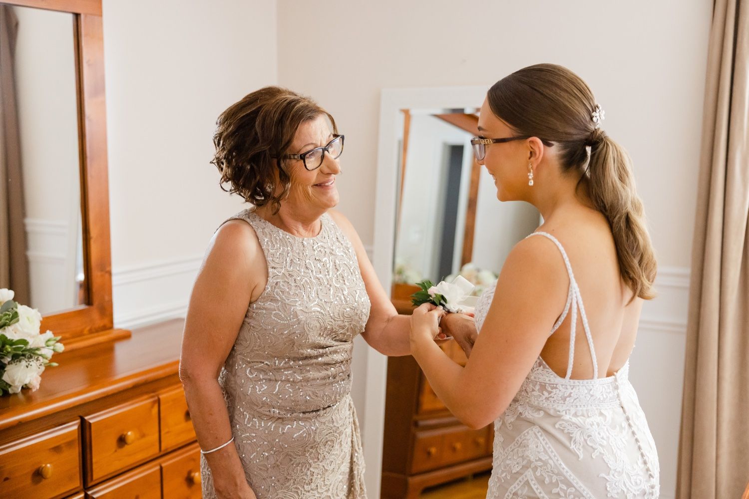 Two people share an intimate moment while getting ready in a bedroom with wooden furniture.