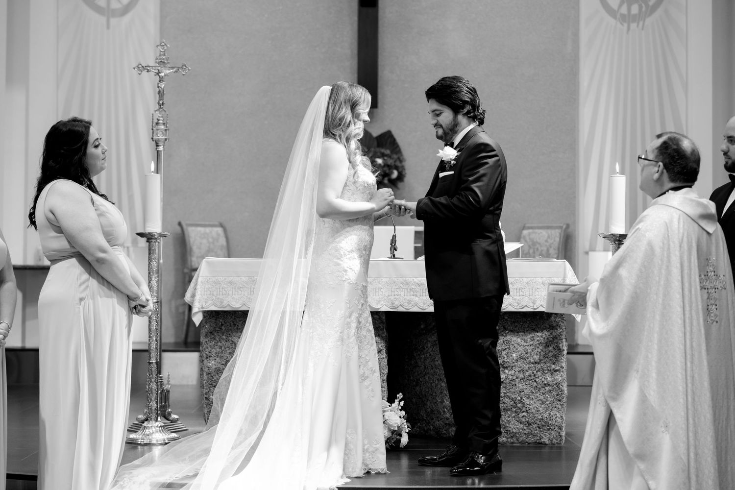 Black and white image capturing intimate moment during Catholic wedding ceremony.