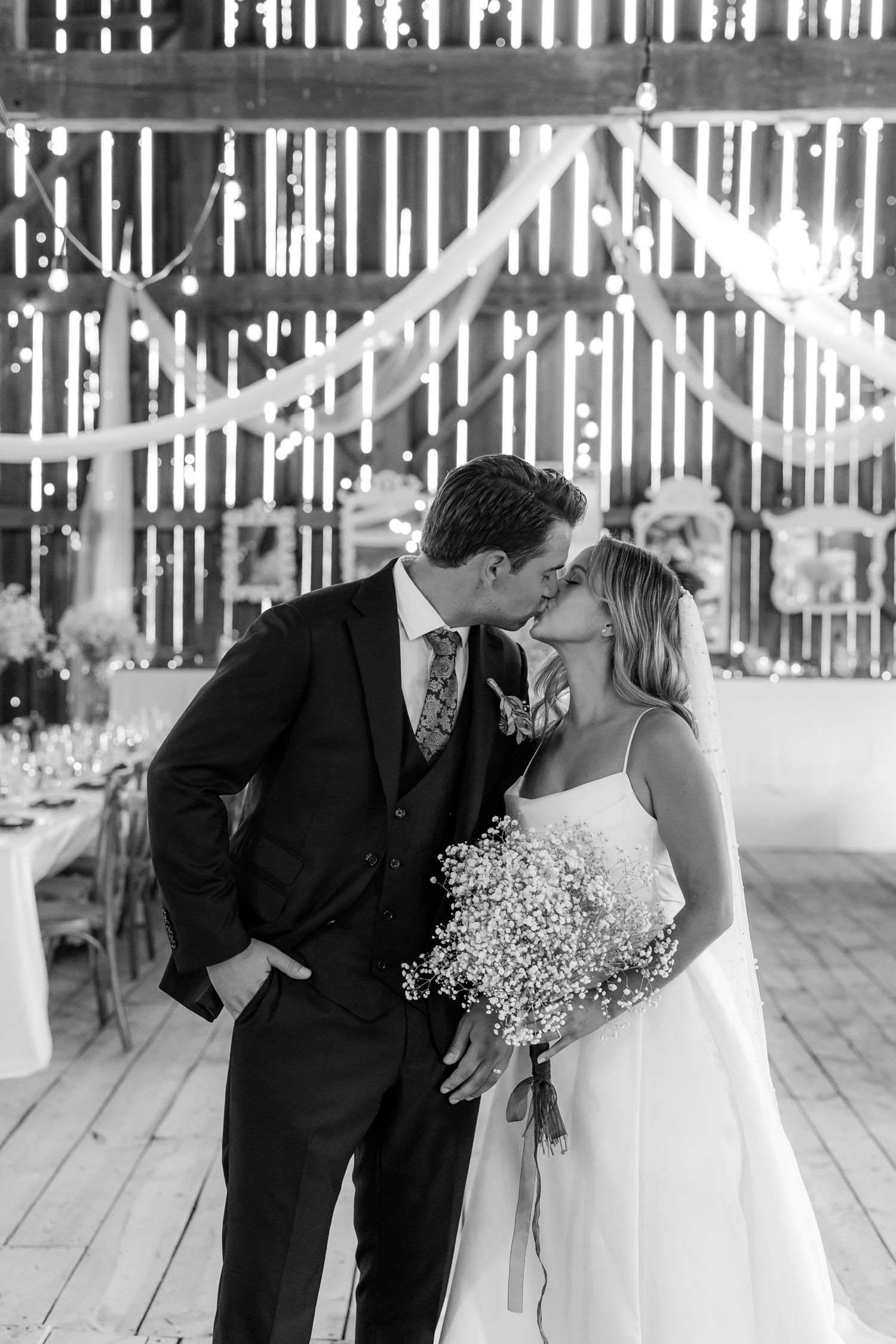 An intimate black and white wedding portrait captured inside a decorated barn venue.
