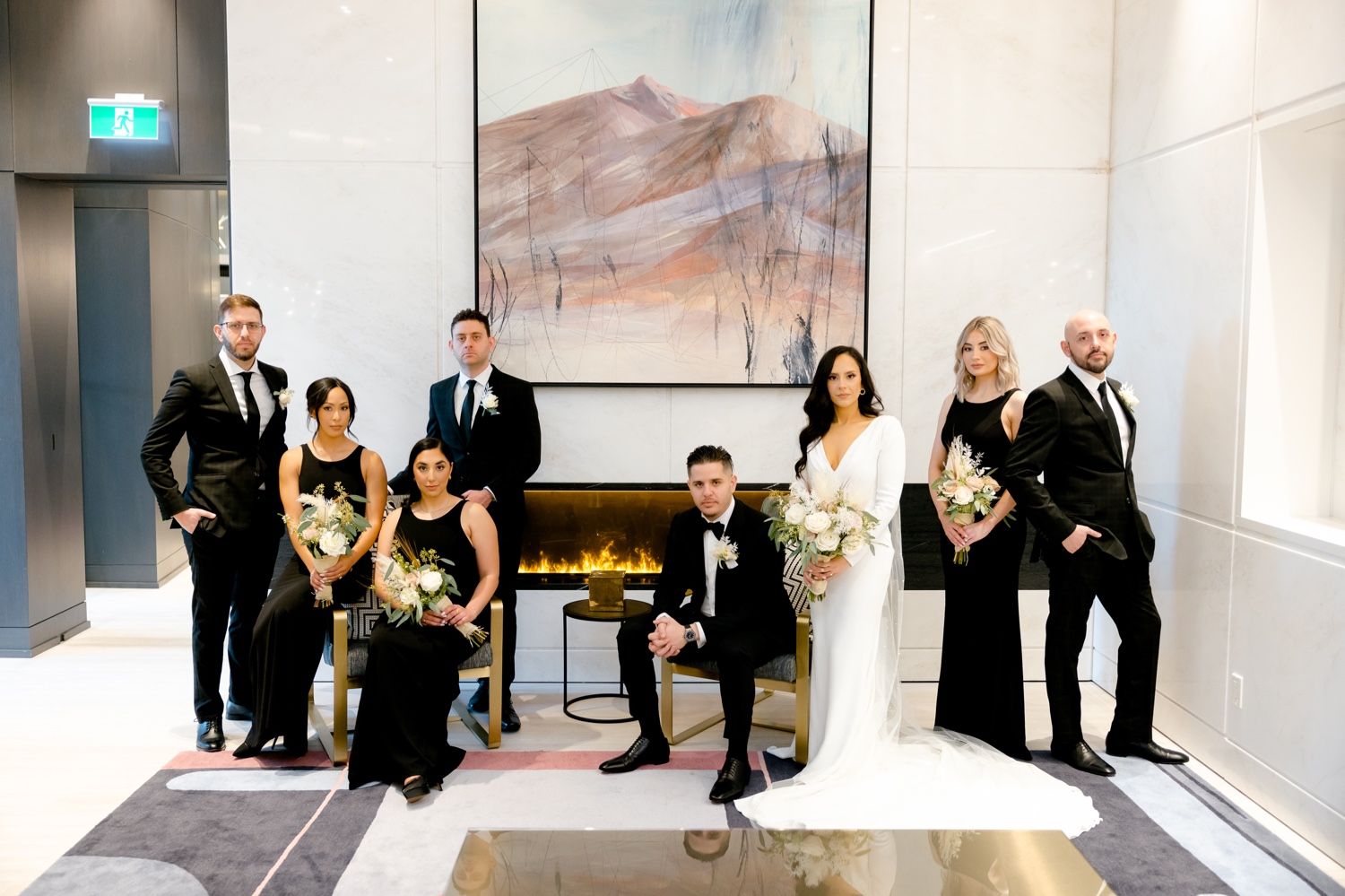 Wedding party poses elegantly by modern fireplace with abstract art and contemporary decor.