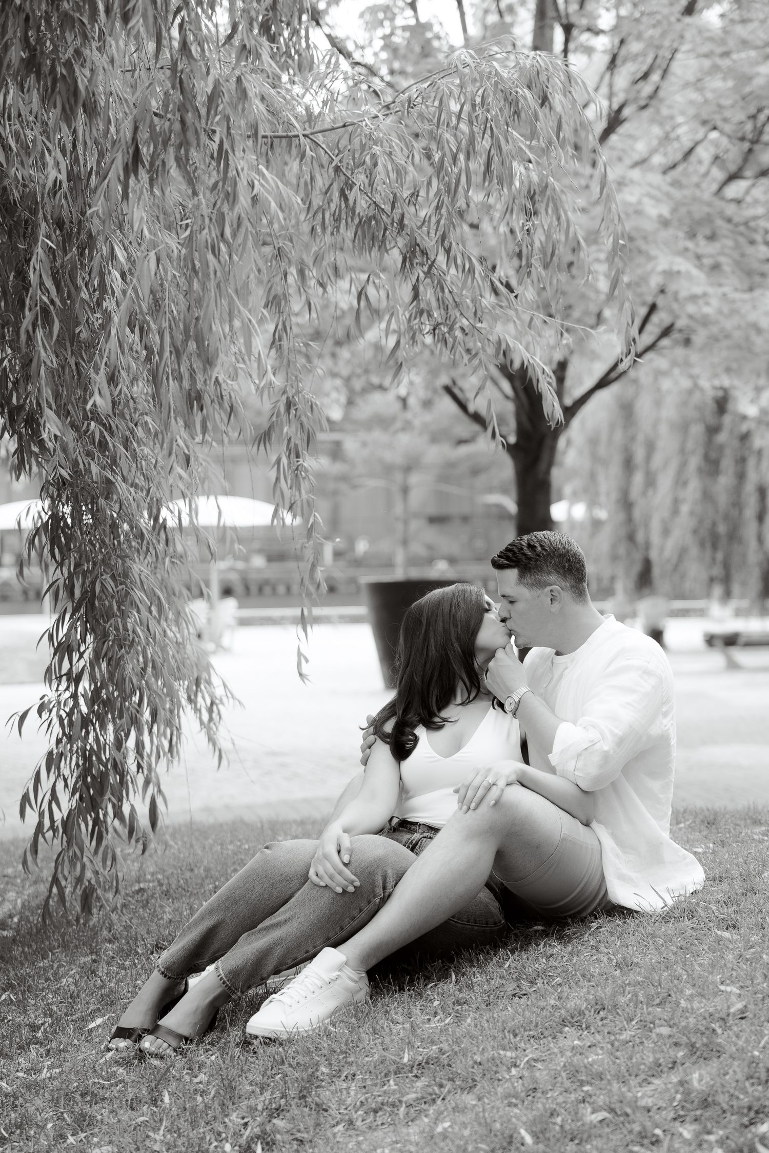 Black and white photo of couple sharing intimate moment under willow tree.