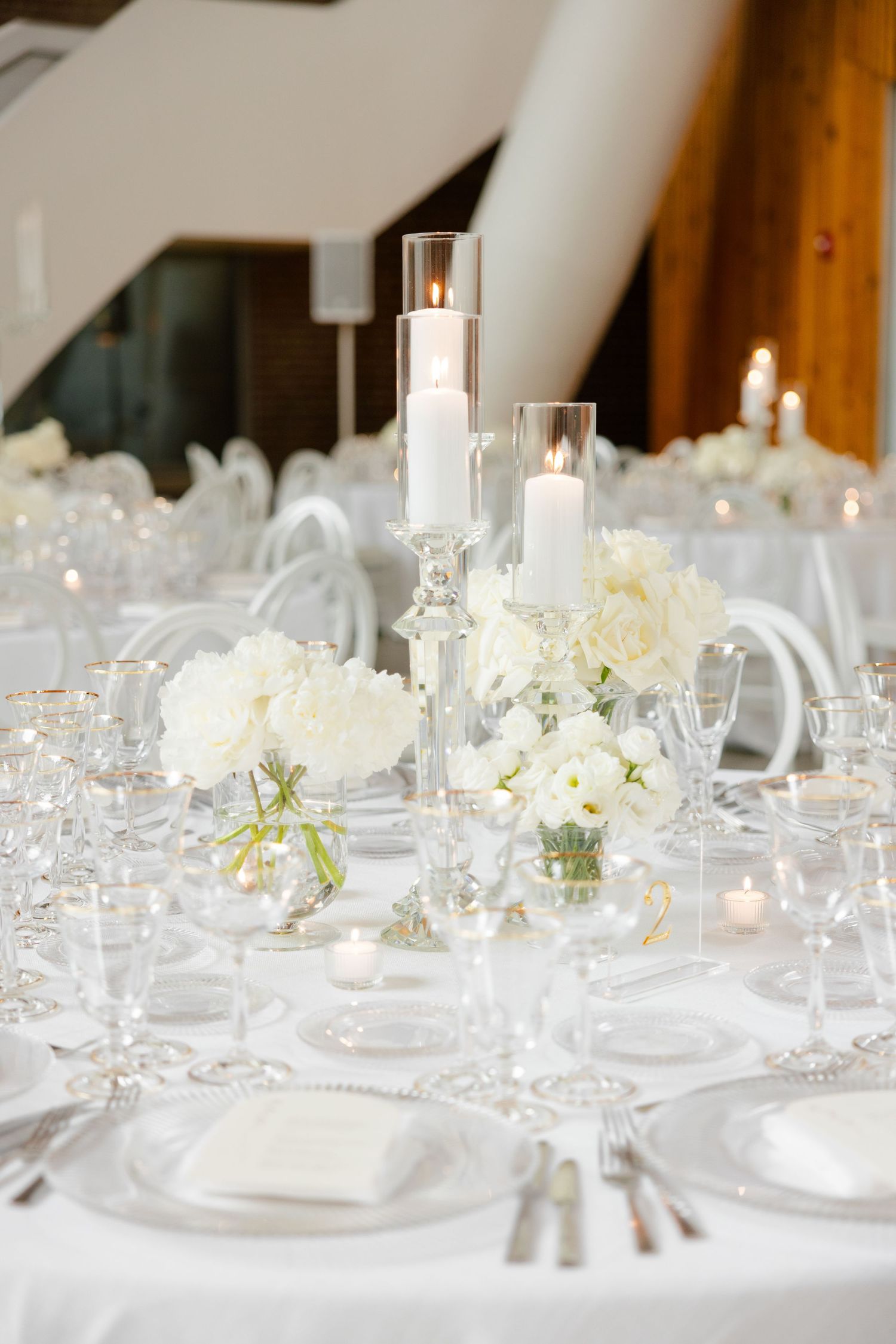 Romantic table decor featuring white floral centerpieces, glass pillar candles, and formal place settings.