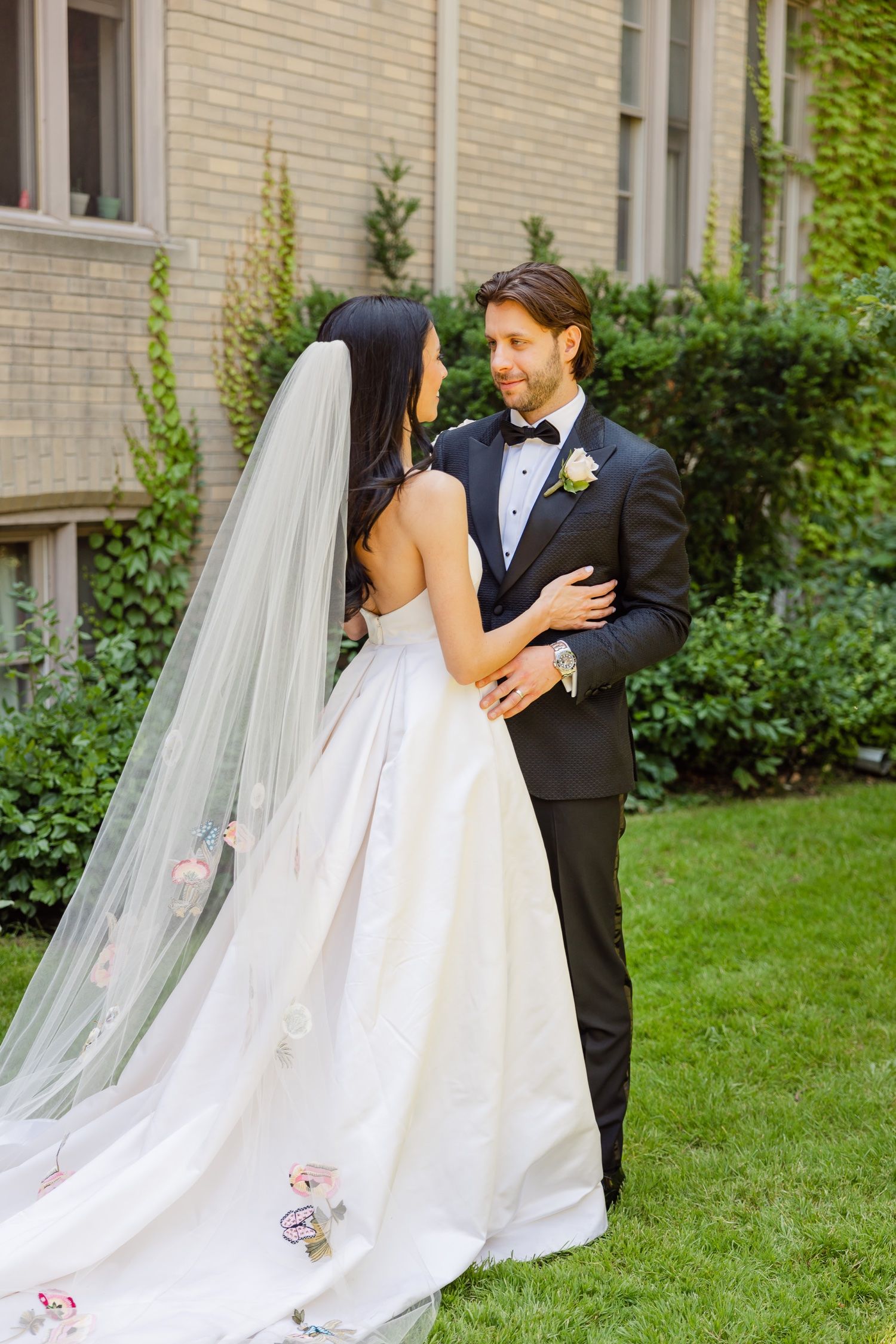 Intimate wedding portrait of a couple in classic black and white attire near an ivy-covered wall.