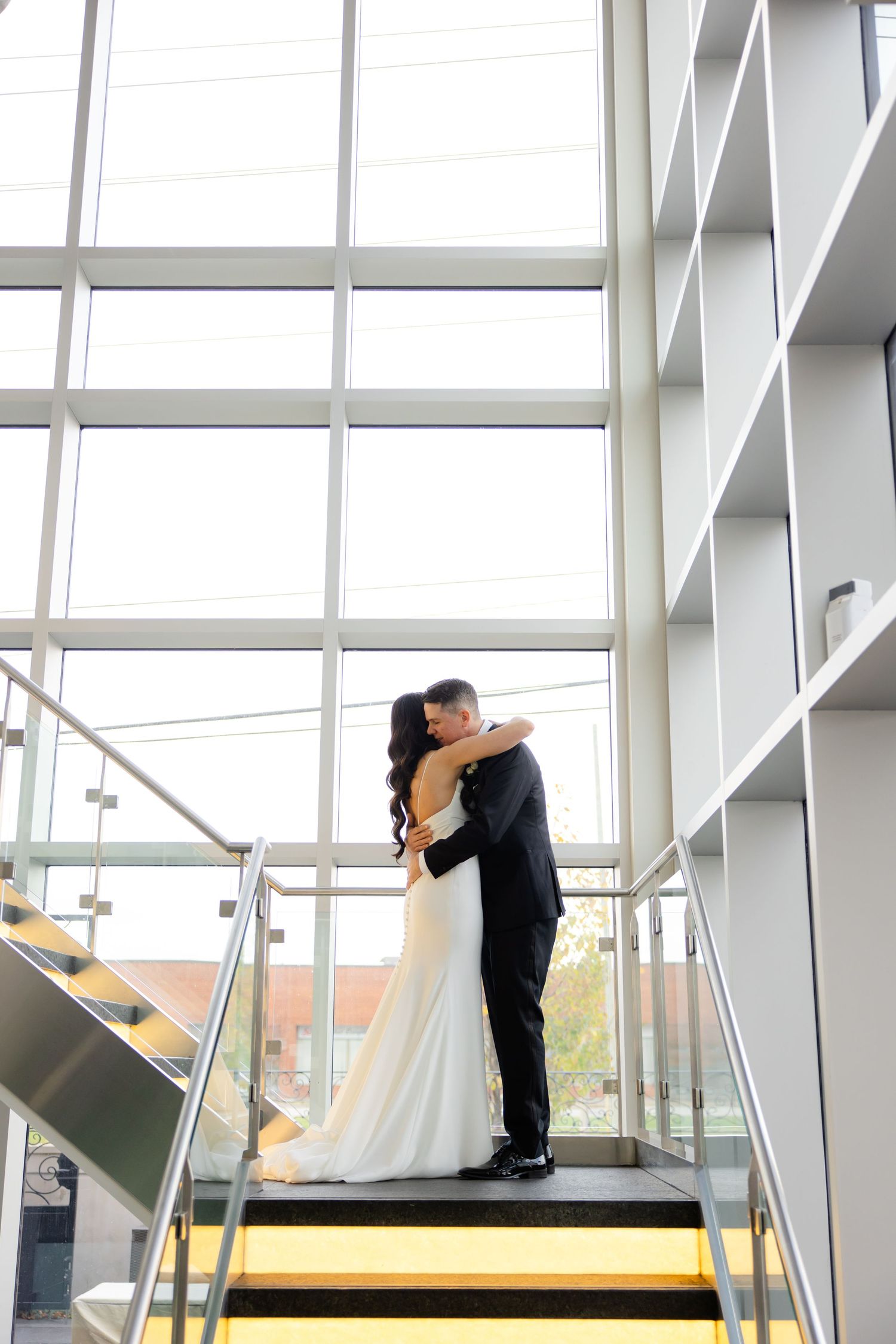 Couple embraces on yellow-striped stairs surrounded by modern architecture and natural light.