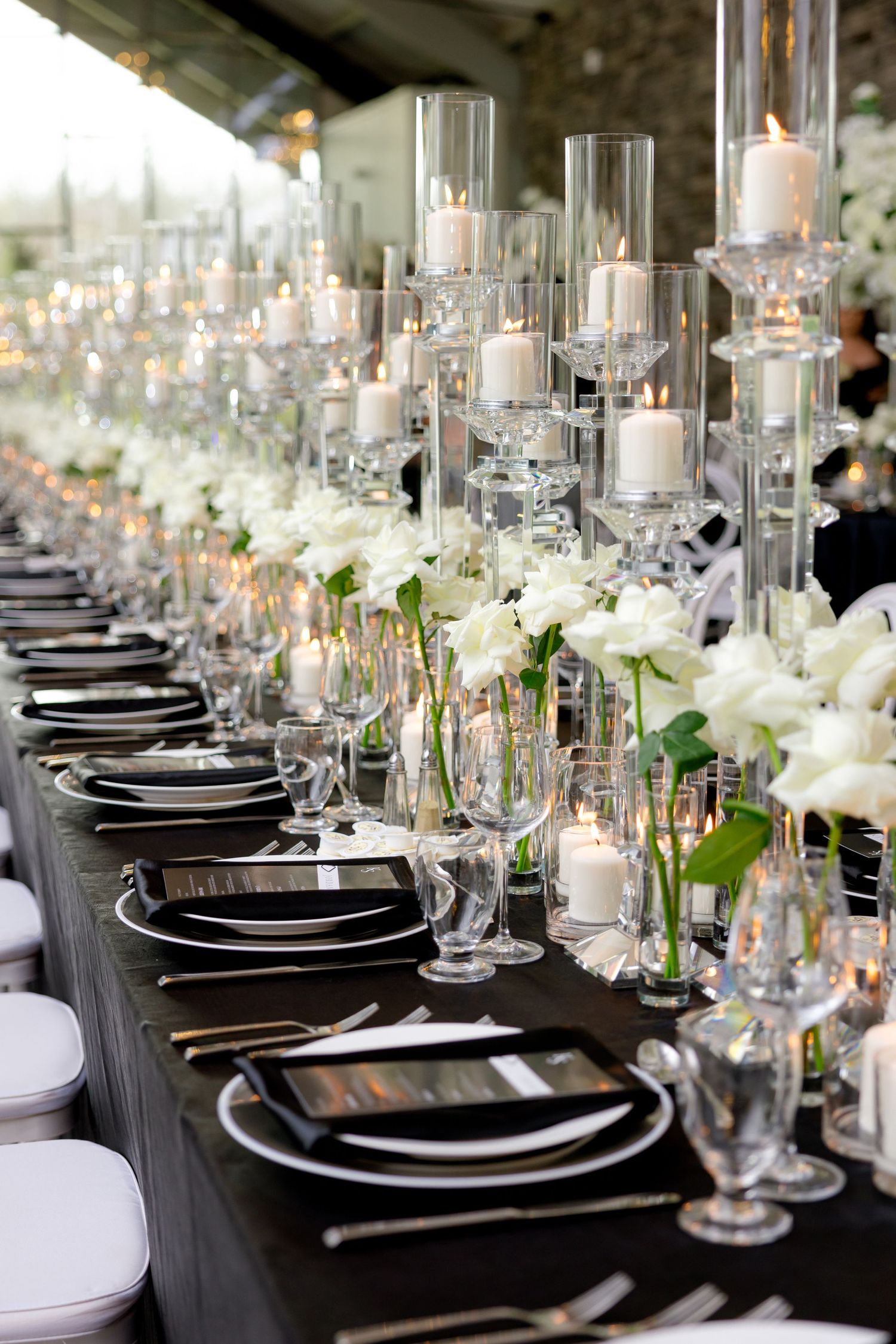 Elegant wedding table setting with black linens, tall glass candle holders, and white floral centerpieces.