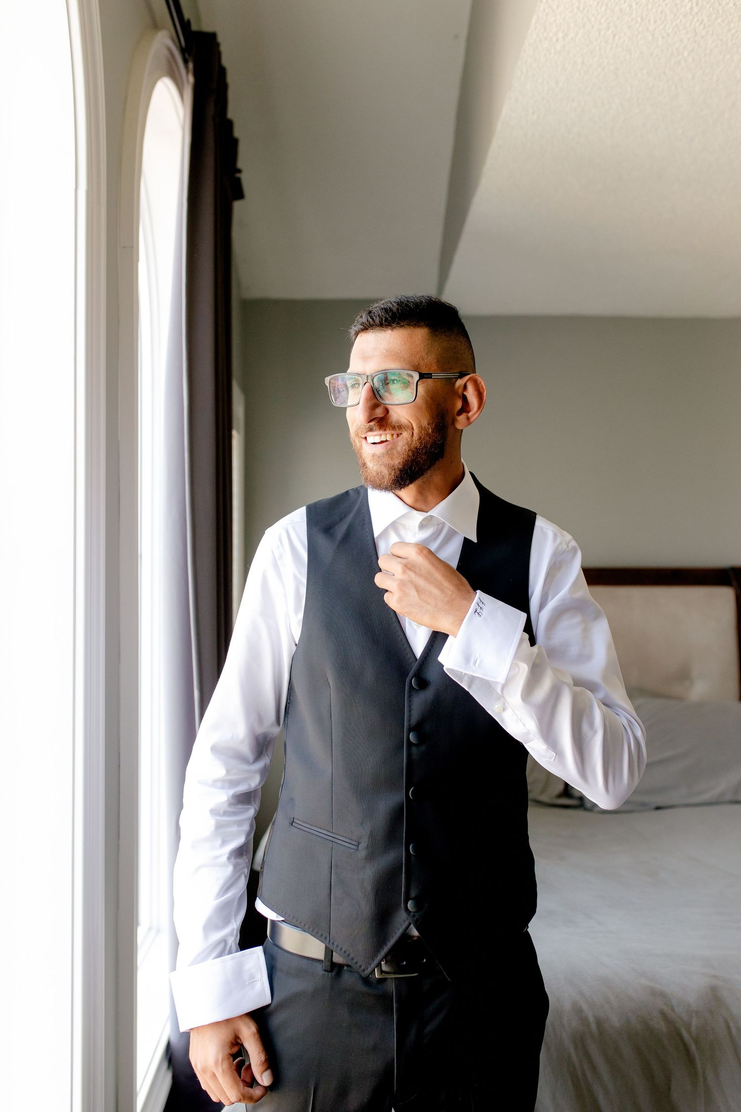 A person adjusts their tie while wearing a formal grey vest and white dress shirt.
