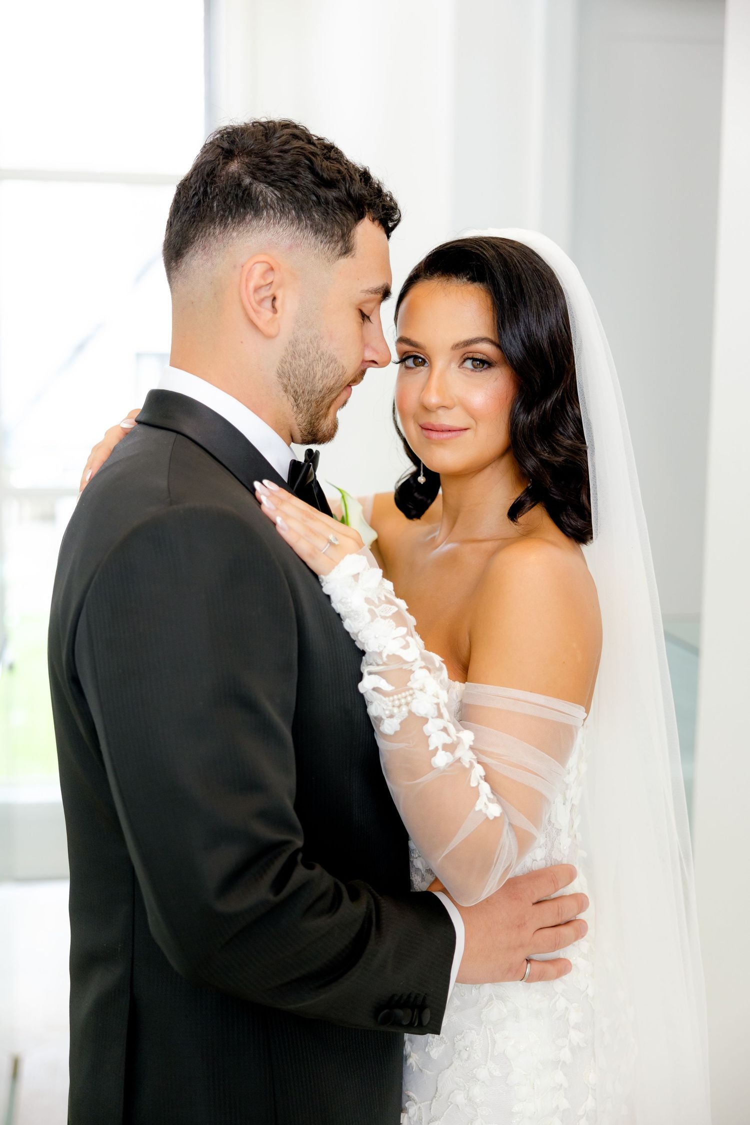 A tender moment between newlyweds as they embrace in front of a bright window.