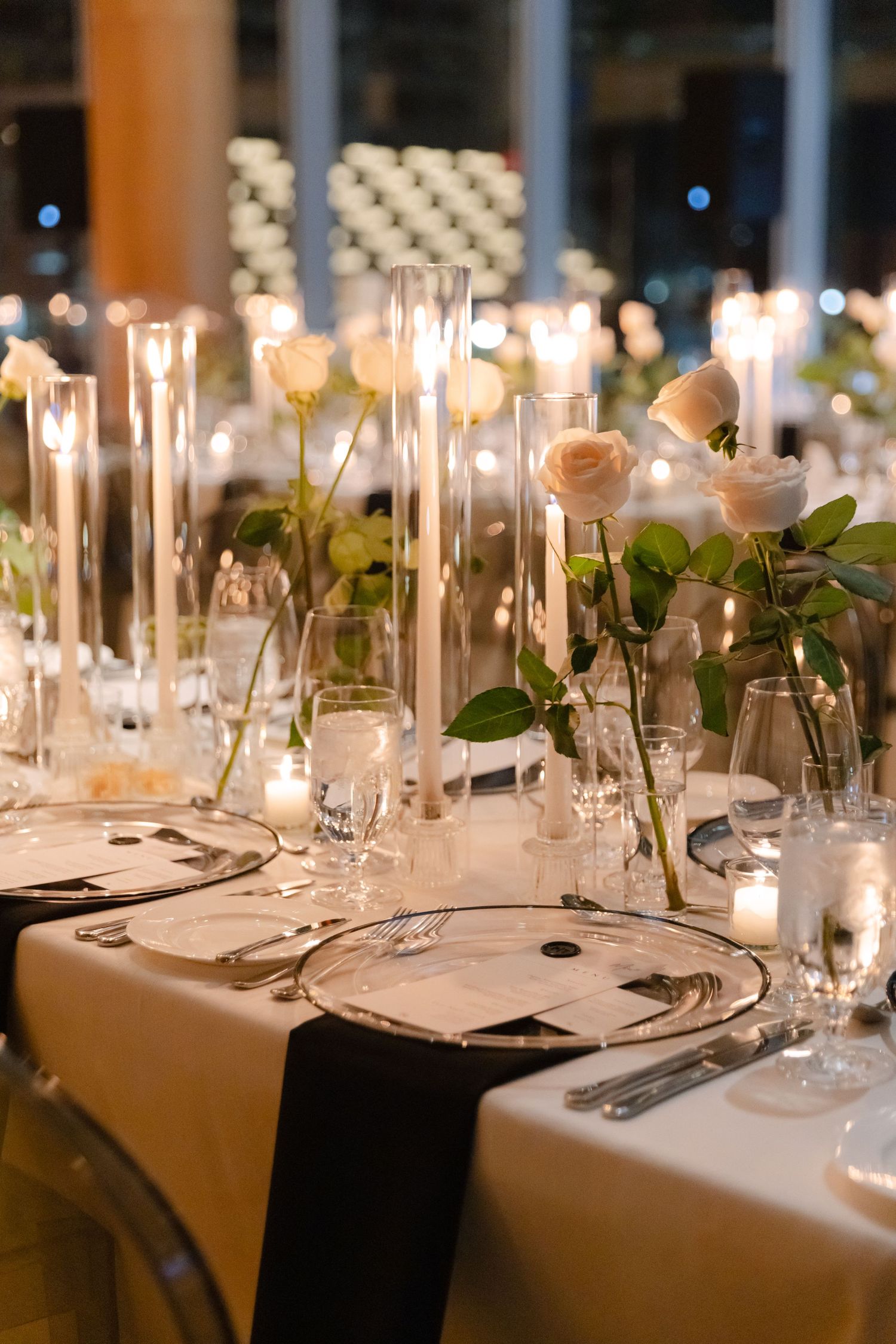 Romantic wedding reception table with candlelit centerpieces, white roses, and place settings.