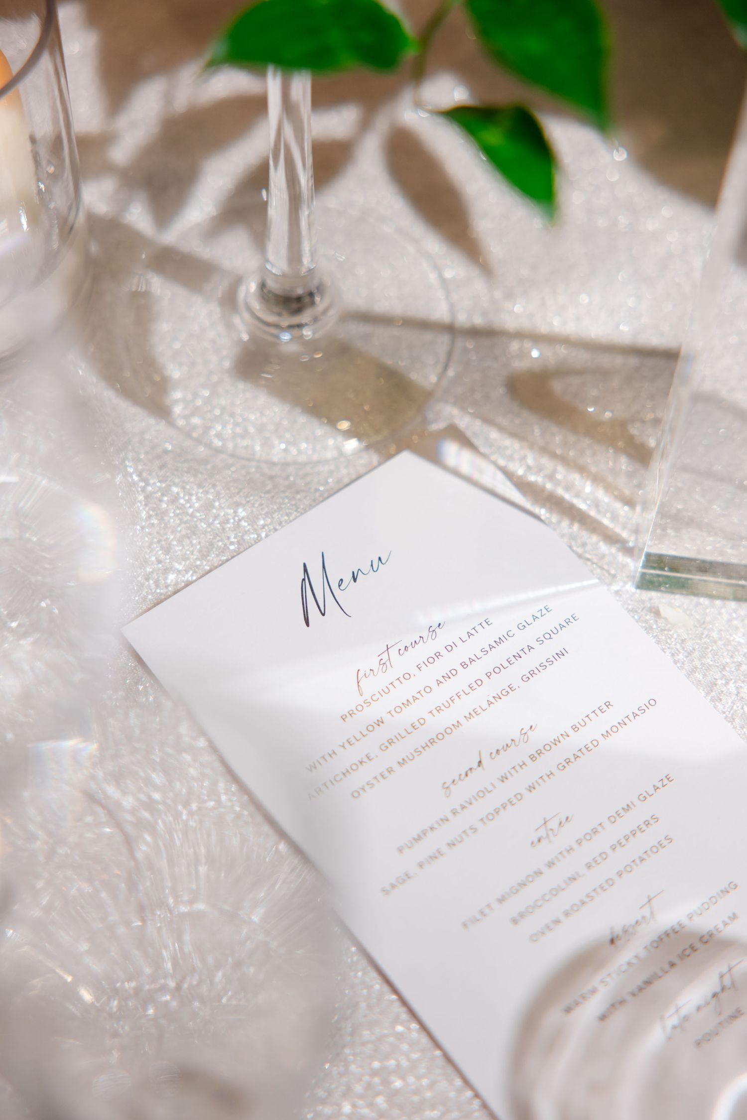 Wedding menu card placed on white textured tablecloth with wine glass casting shadow.