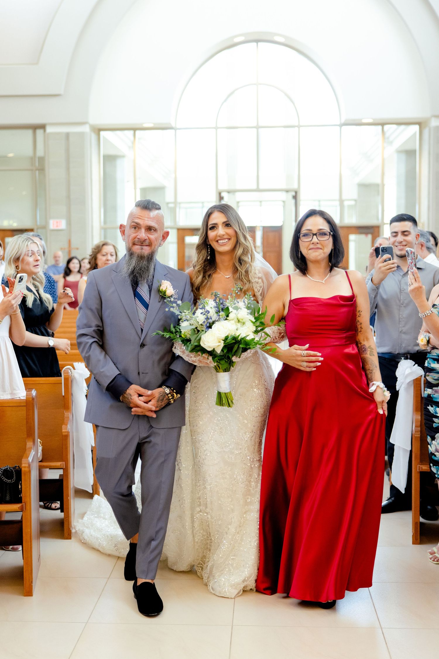 A wedding party walks down the church aisle while guests capture photos from the pews.